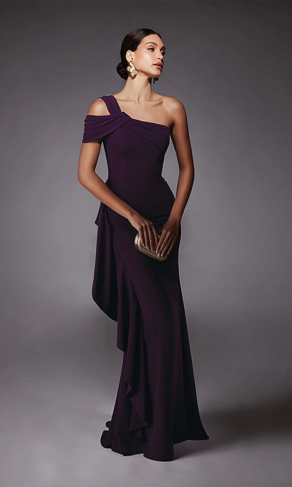 A woman models the Alyce 27705 long formal dress, a one-shoulder, floor-length dark purple gown, styled with a gold clutch and statement earrings against a neutral background.