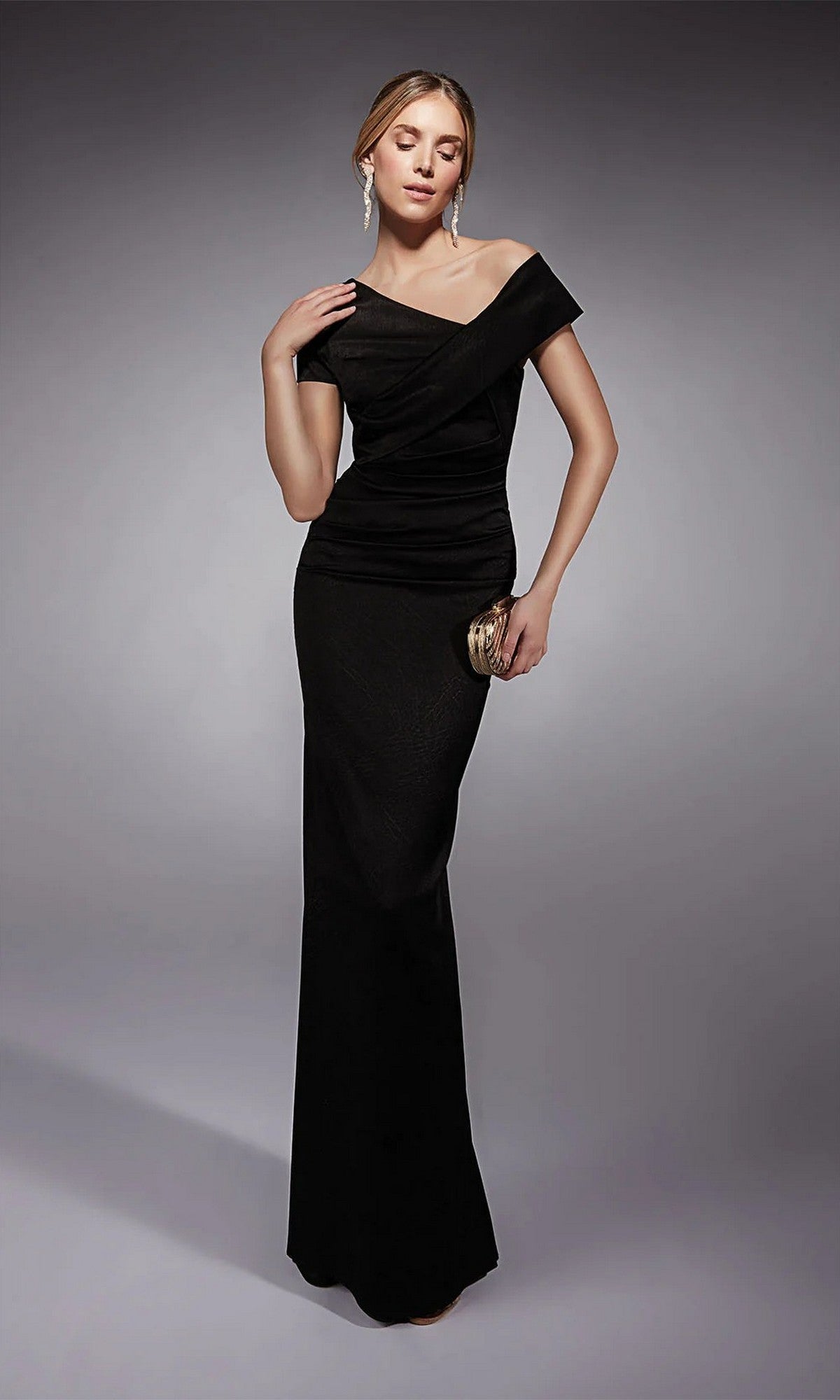 A woman models the Long Formal Dress: Alyce 27710, an elegant off-the-shoulder black gown, holding a small clutch and posing against a neutral gray background.