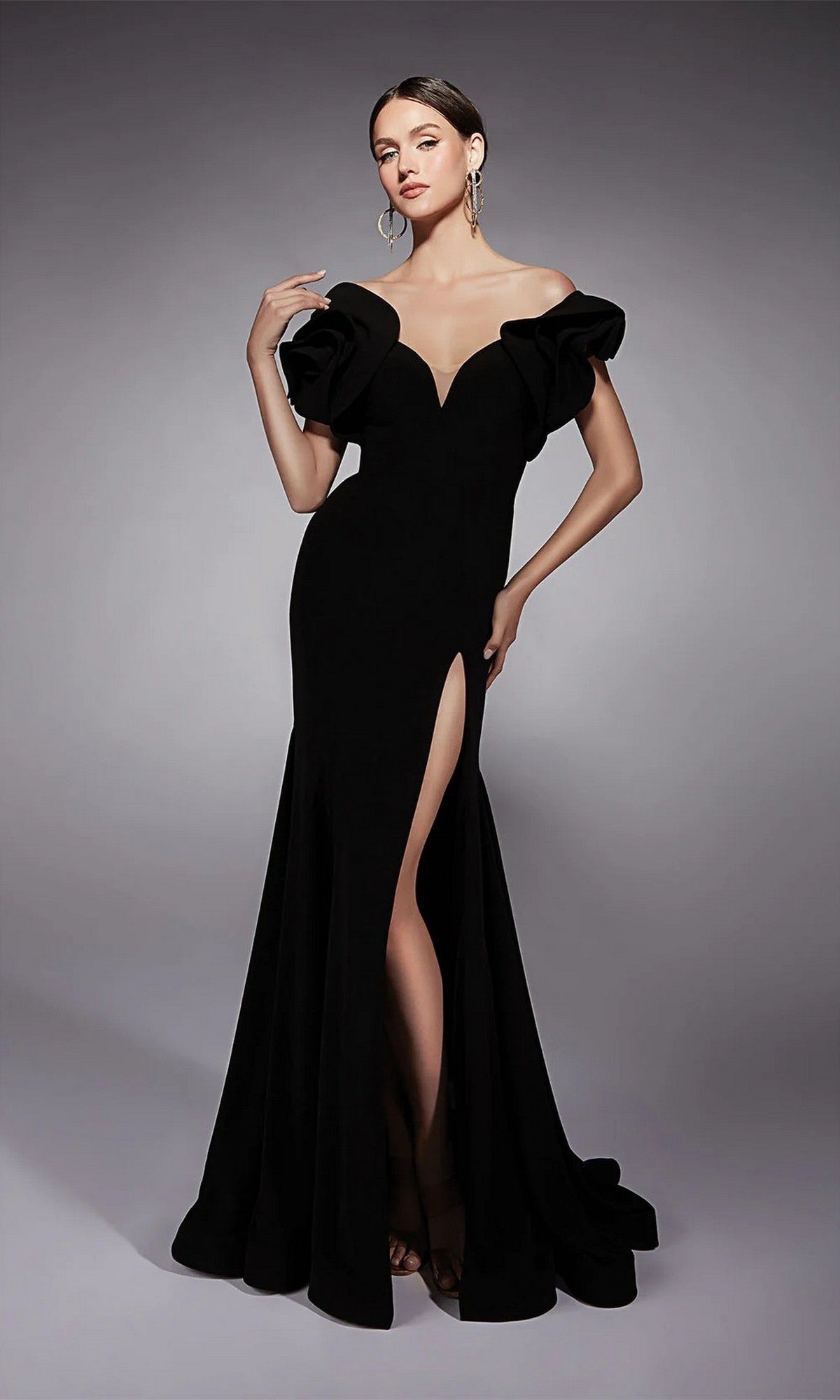 A woman models the Alyce 27714 long formal dress in black—an off-the-shoulder gown with ruffled sleeves, a thigh-high slit, and a sleek sheath silhouette—posed against a plain gray background.