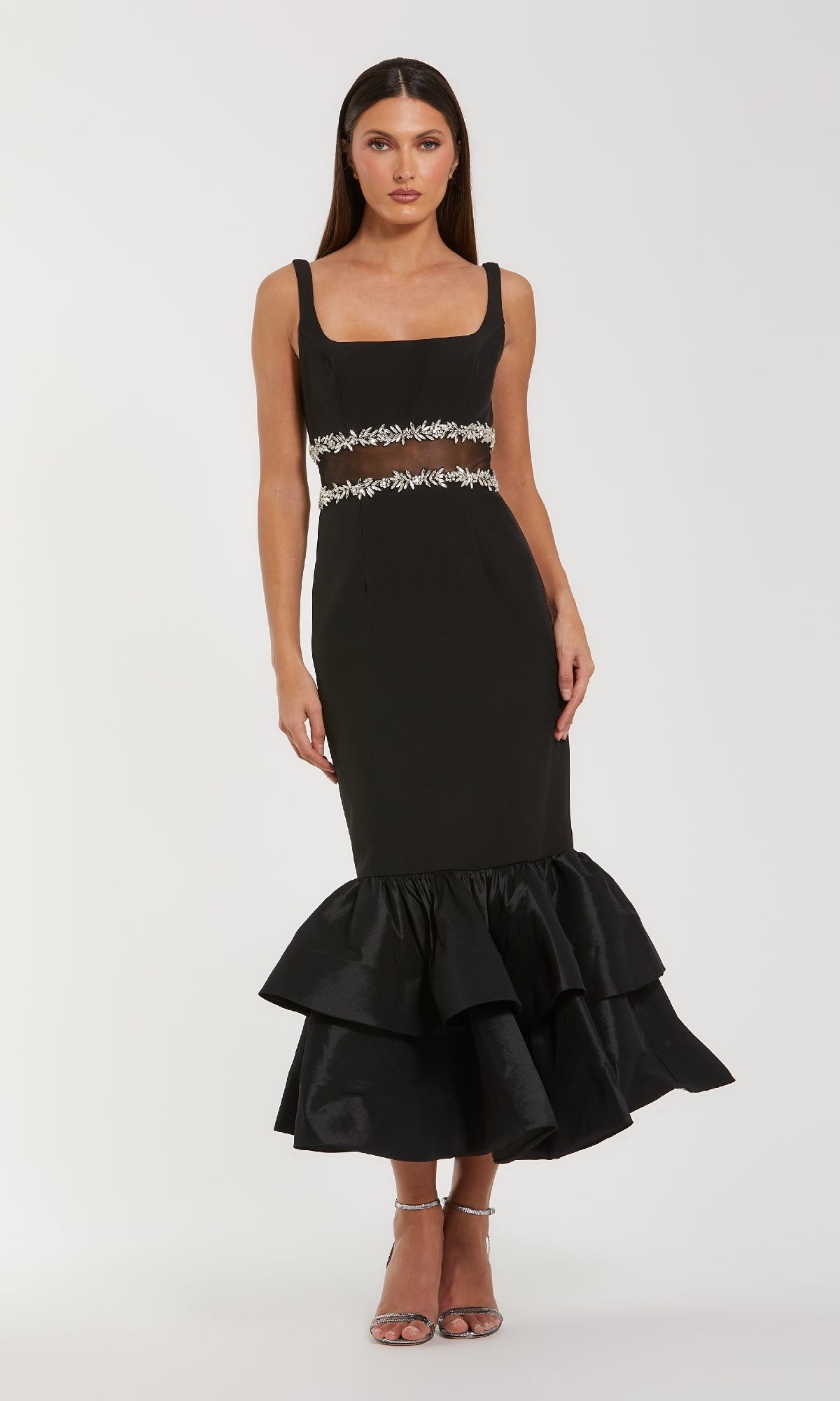 Woman wearing a black evening gown with a sheer waistline and a flared tiered hemline on a white background