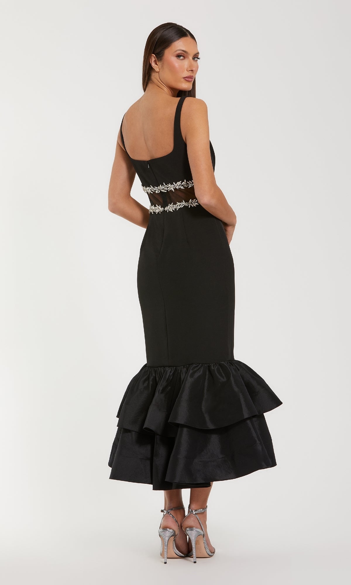 Woman showing the back of a black evening gown with a tiered flared hemline.