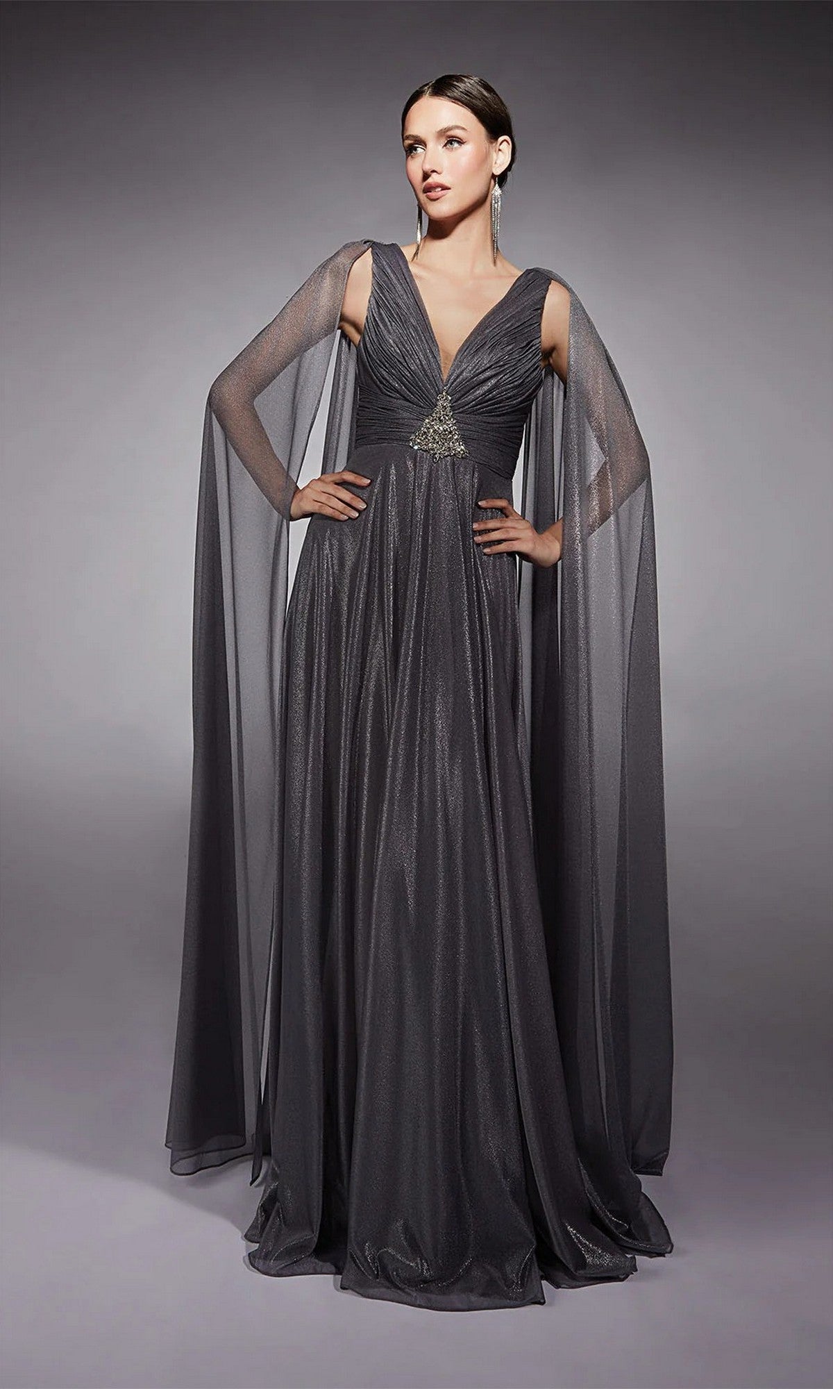 A woman models the Alyce 27720 long formal dress in gunmetal, featuring metallic chiffon, sheer cape sleeves, and a deep V neckline—an elegant mother-of-the-bride choice against a plain gray backdrop.
