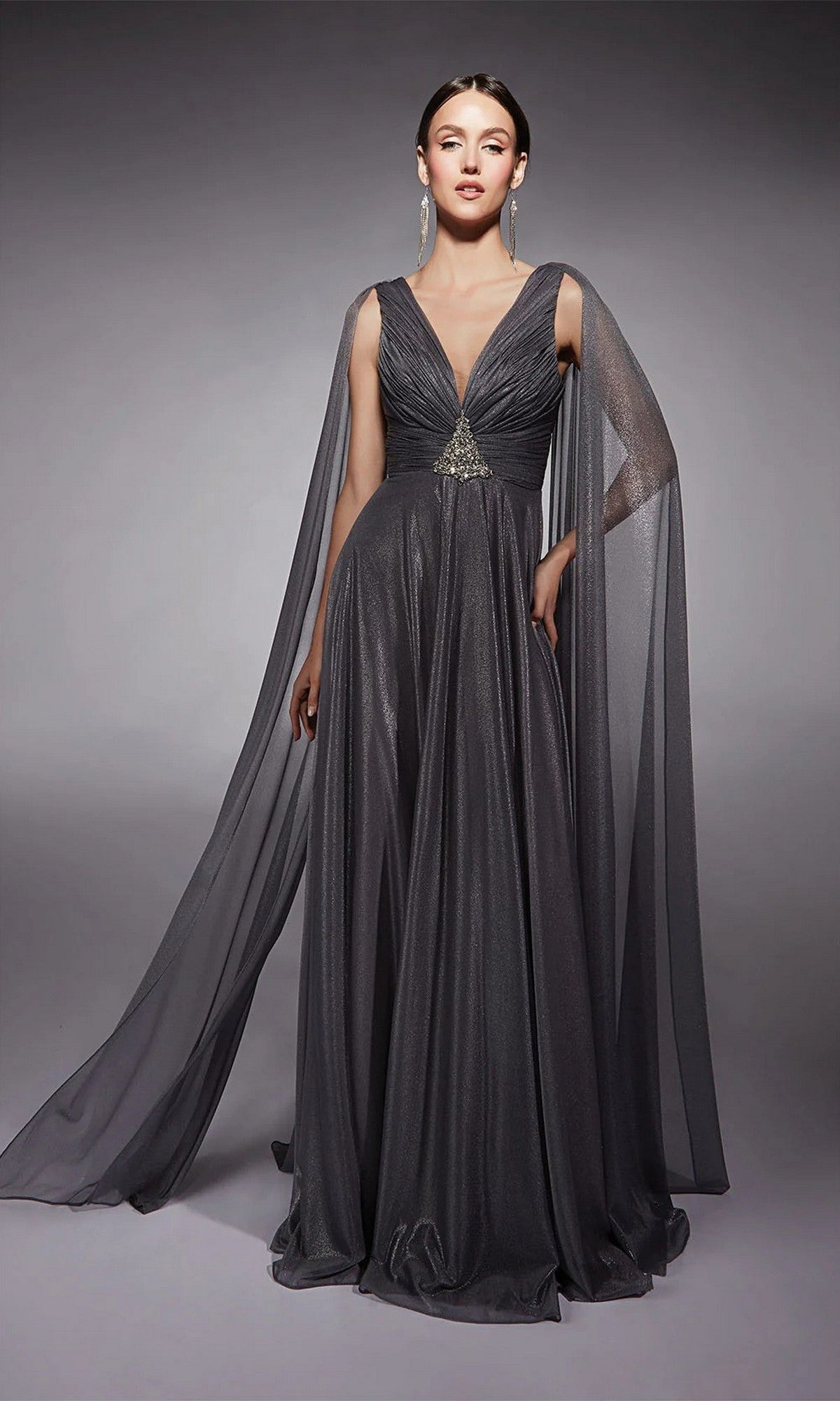 A woman models the Alyce 27720 long formal dress, a metallic chiffon gown with deep V-neck, cinched waist, jeweled accents, and sheer floor-length cape sleeves—an elegant mother-of-bride choice against a plain gray backdrop.