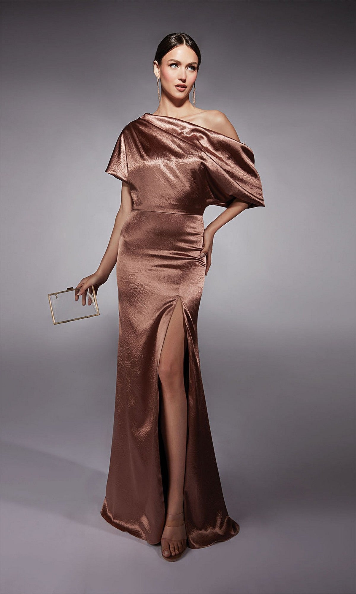 Woman in a sultry blush Alyce 27721 long formal one-shoulder dress with thigh-high slit, holding a small rectangular clutch, standing against a plain gray background.