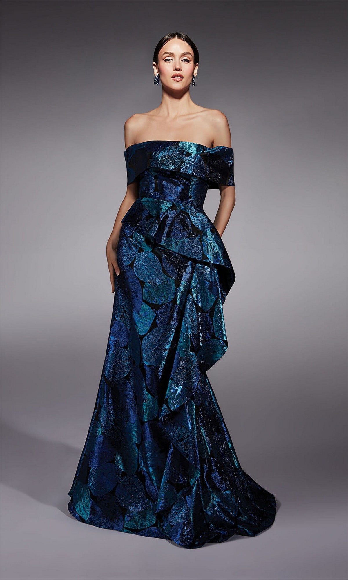 A woman models the Alyce 27736 long formal dress—an off-the-shoulder, floor-length dark blue gown with a textured leaf pattern, asymmetrical draping, and a fit-and-flare silhouette against a gray backdrop.