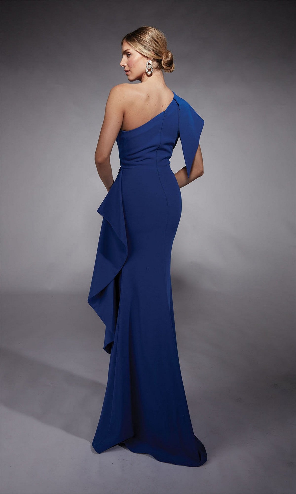 A woman in a fitted, floor-length Alyce 27738 long formal dress in royal blue stands facing away against a neutral background.