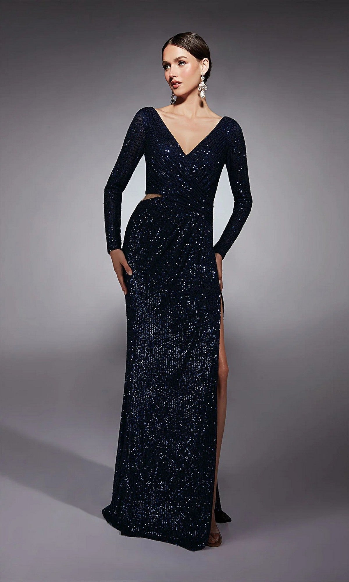 A woman wears the Alyce 27741 long formal dress in Midnight, featuring sequins, a deep V-neck, cut-out waist, thigh-high slit, and long sleeves as she poses against a plain gray background.