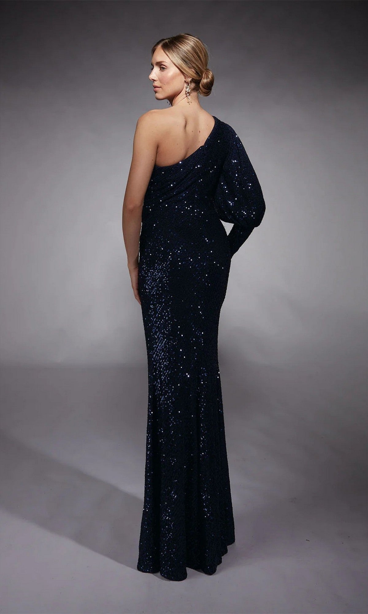 Woman wearing the Long Formal Dress: Alyce 27742 in dark blue sequins stands facing away, looking over her shoulder against a gray background—ideal for elegant evening occasions.