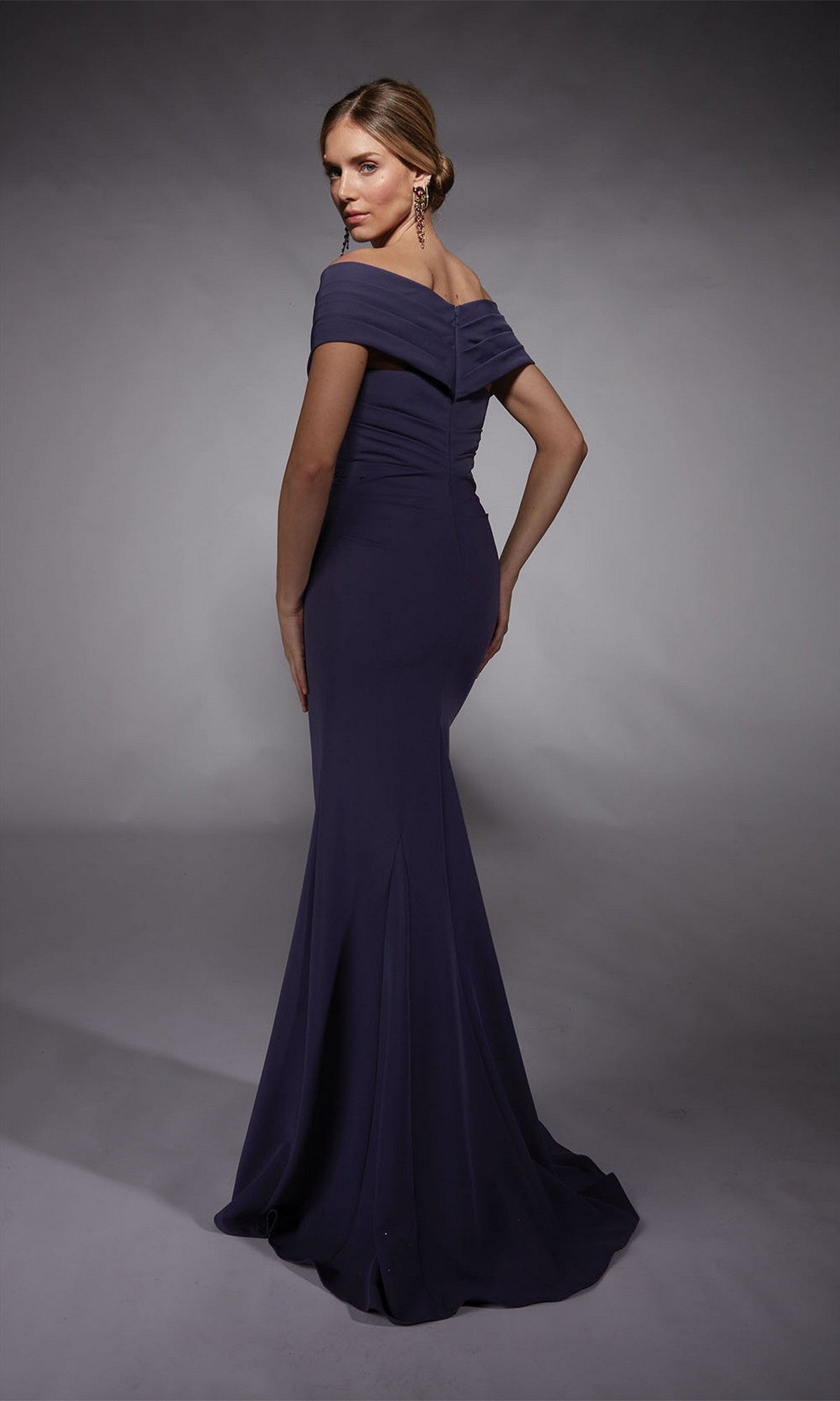 A woman poses in the Alyce 27745, a long formal dress with an off-the-shoulder neckline, fitted silhouette, and ruched bodice—ideal for prom night elegance.