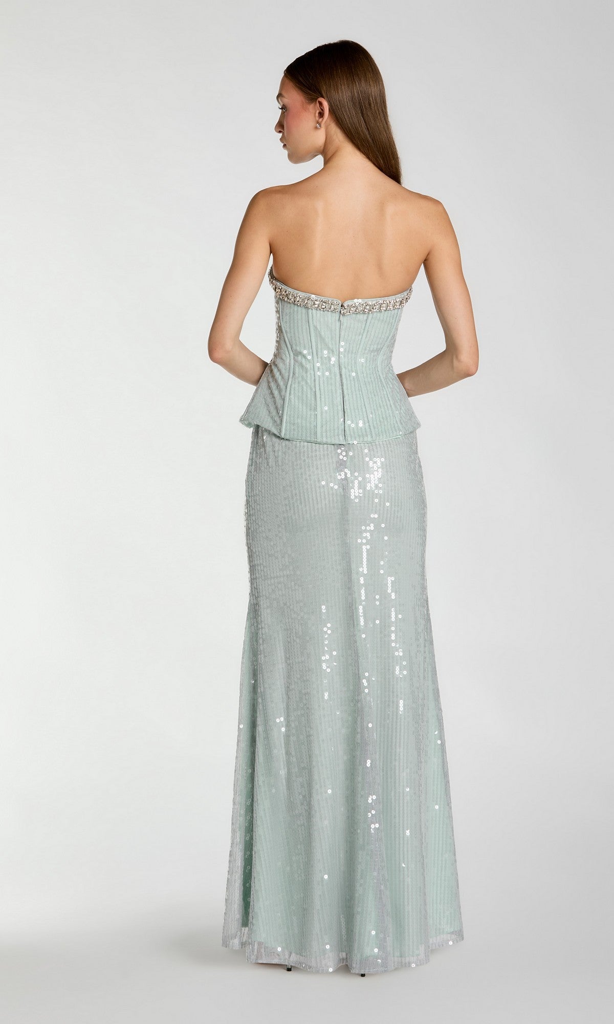 A woman stands with her back to the camera, wearing the Mac Duggal 27776 long formal dress—a strapless, light green sequin gown featuring a fitted bodice and an elegant floor-length skirt for an unforgettable evening look.