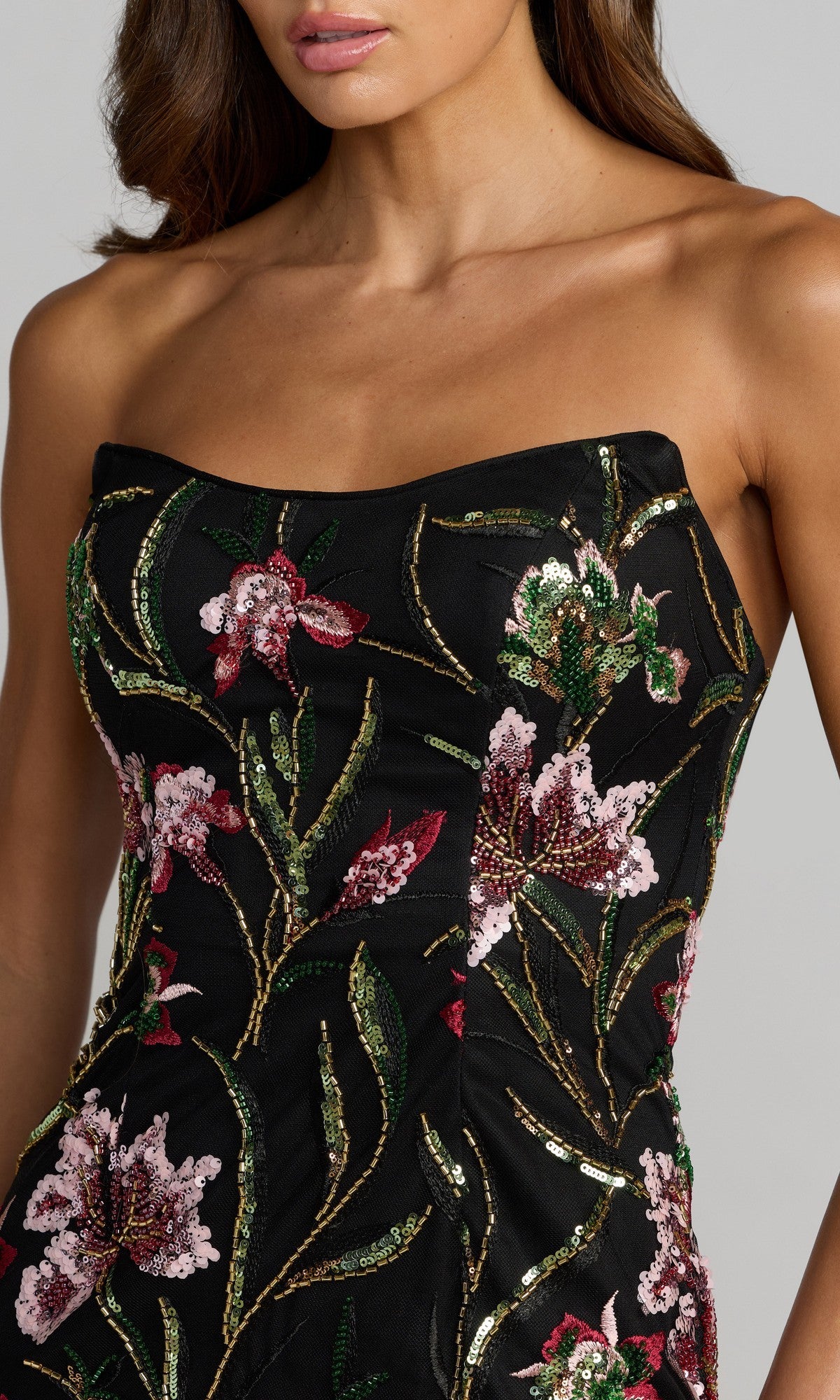 A woman is wearing the Mac Duggal 27814 long formal dress—a strapless black gown featuring pink, green, and gold floral embroidery—shown from the shoulders to mid-torso.