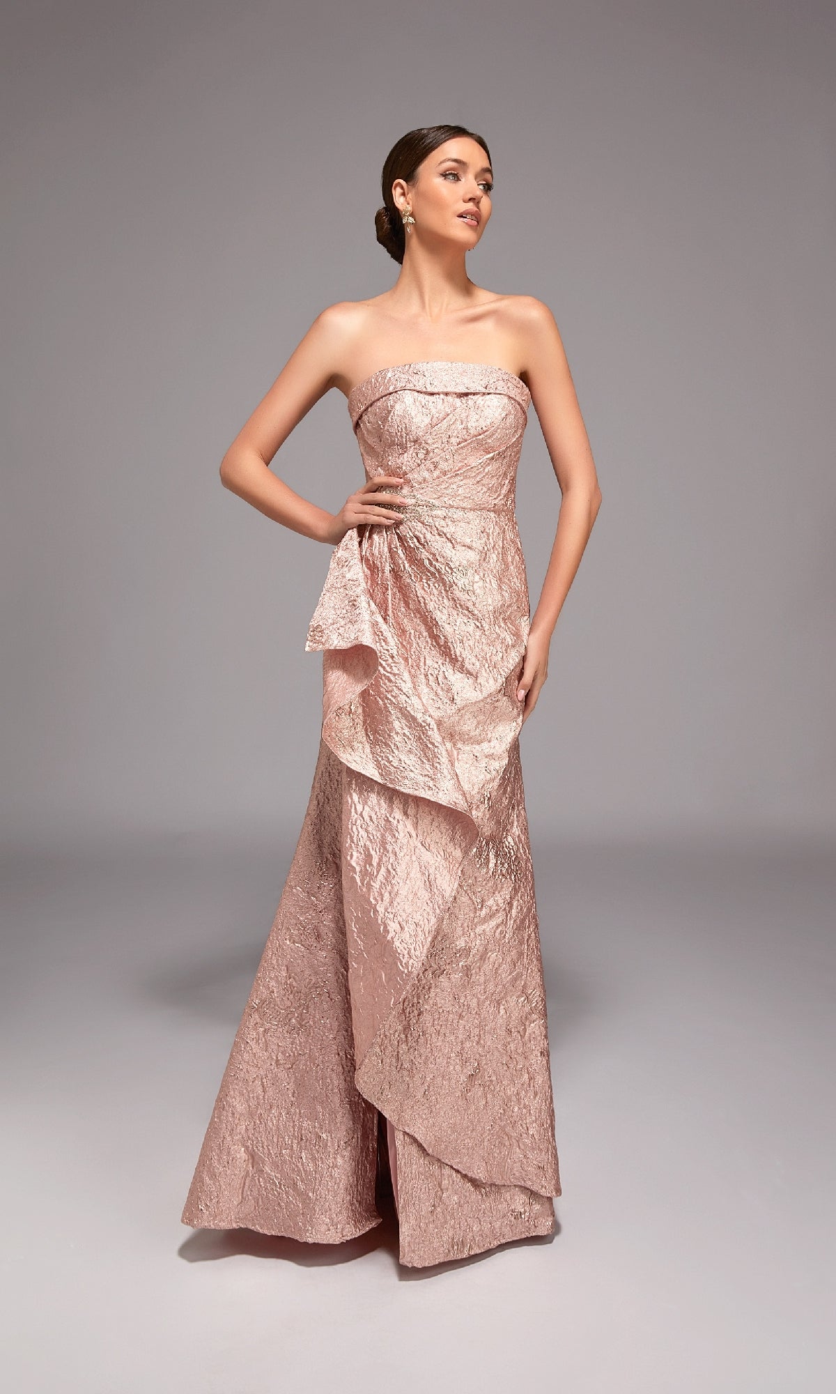 A woman stands against a plain gray background wearing the Alyce 27818 Long Formal Dress, a floor-length strapless jacquard blush pink gown with ruffled details—ideal for special occasions.