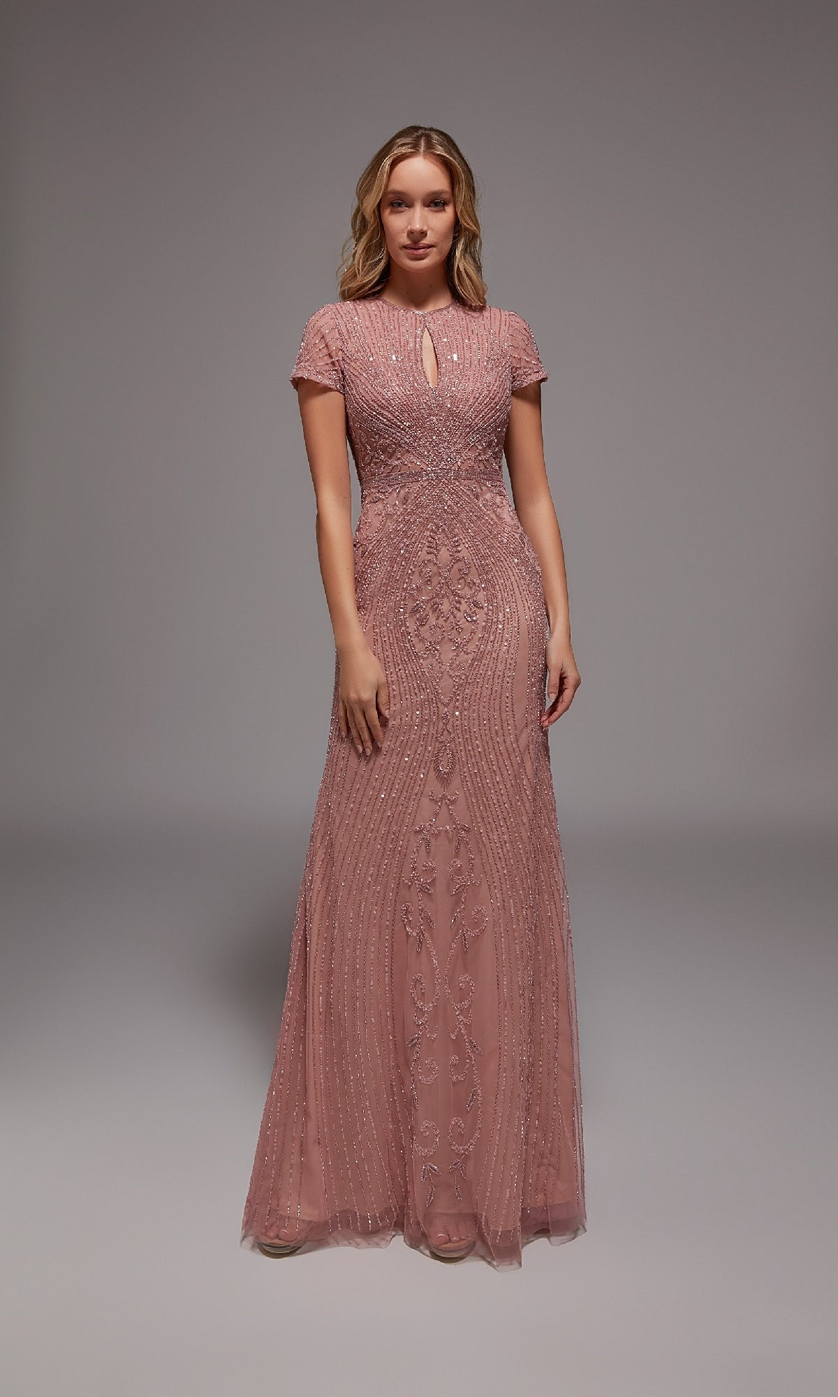 A woman faces forward in a Alyce 27823 long formal dress, dusty rose, floor-length with short sleeves, intricate beadwork, and a keyhole neckline, set against a plain gray background.