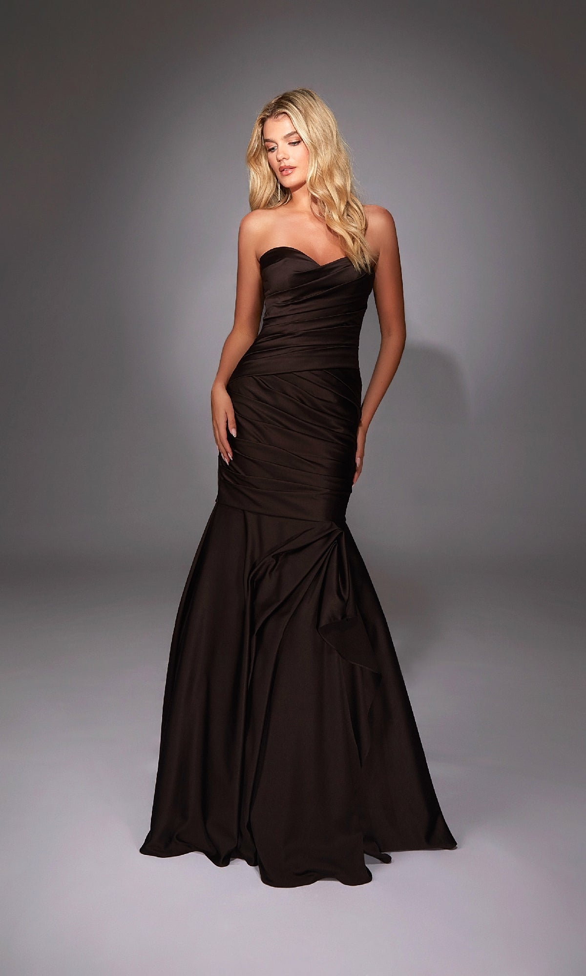 A woman wearing the Alyce 27836 long formal dress, featuring a strapless sweetheart neckline and fitted mermaid skirt, stands against a softly lit plain background.