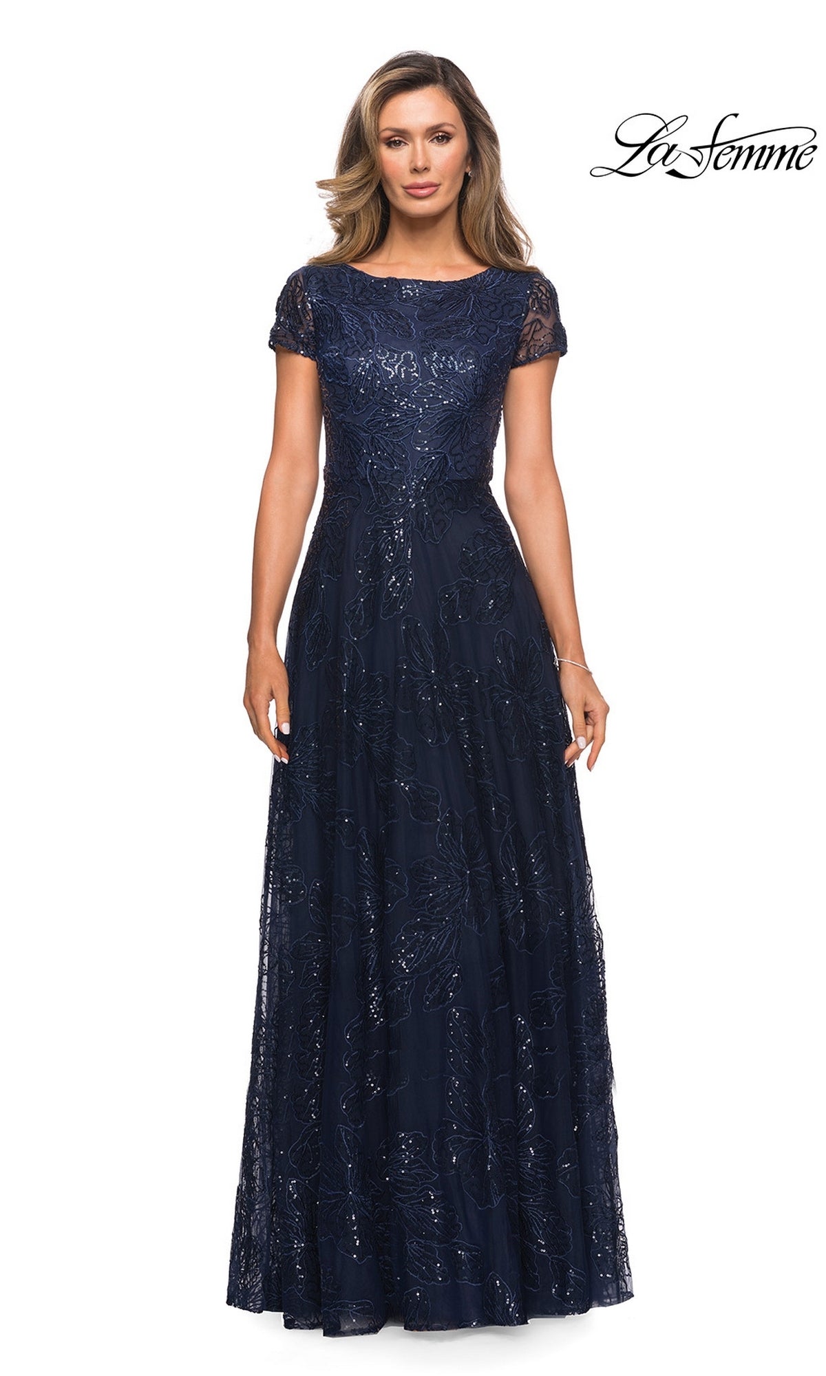 A woman wearing a navy, floor-length La Femme 27837 formal dress with short lace sleeves and an embroidered, sequined overlay.