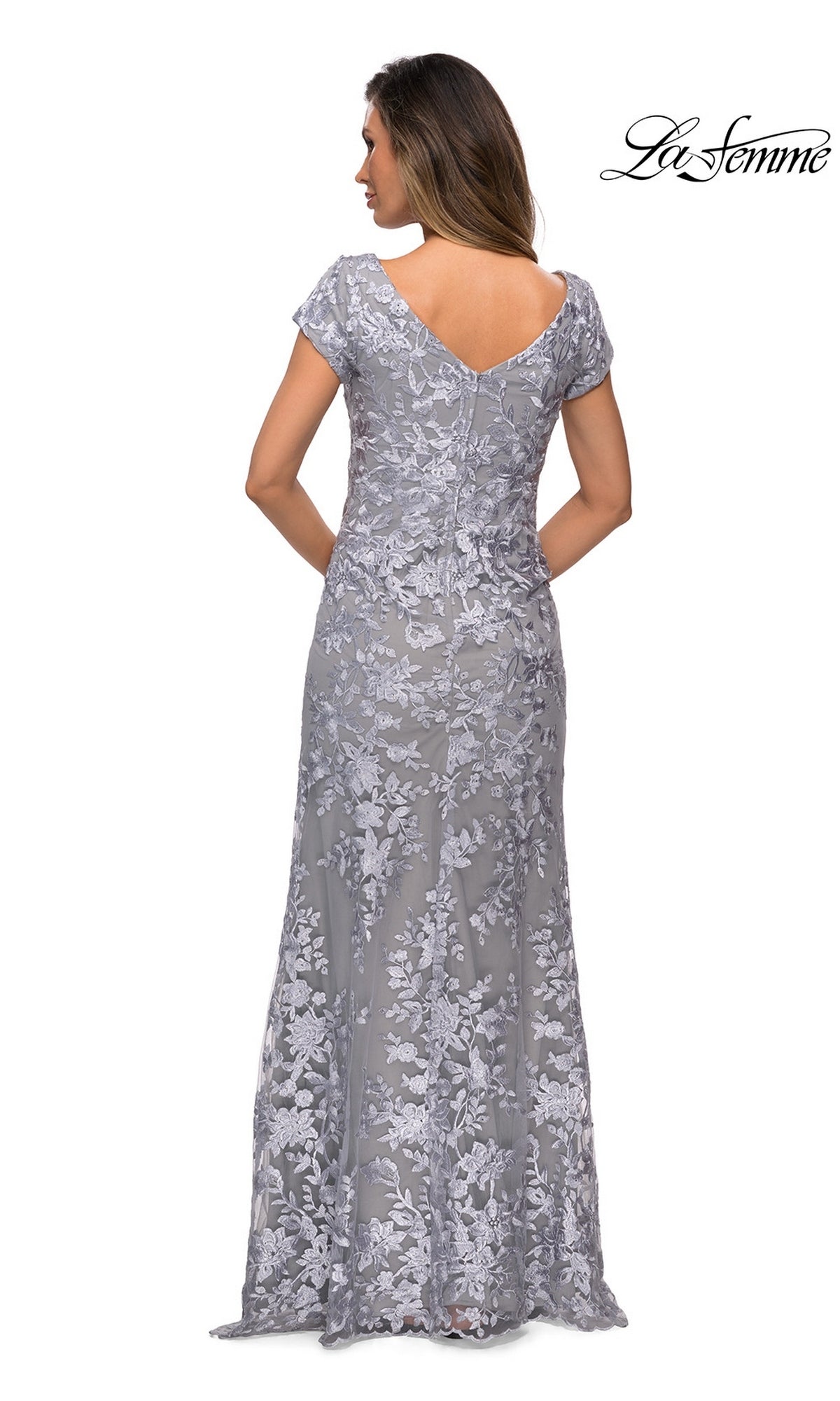 Woman in a floor-length, short-sleeve silver lace Long Formal Dress: La Femme 27842 with floral embroidery and sheath skirt, back view. La Femme logo top right.