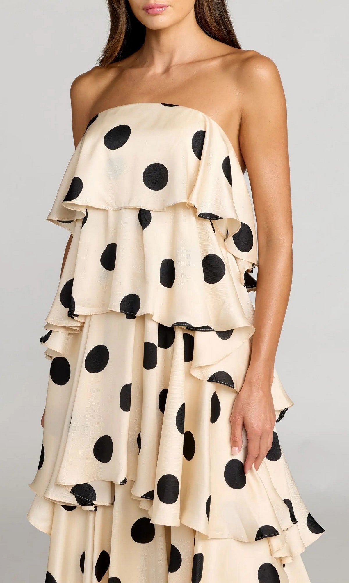 A woman stands against a plain background wearing the Mac Duggal 27845 long formal dress—a strapless beige polka-dot charmeuse gown featuring large black dots and layered ruffles.