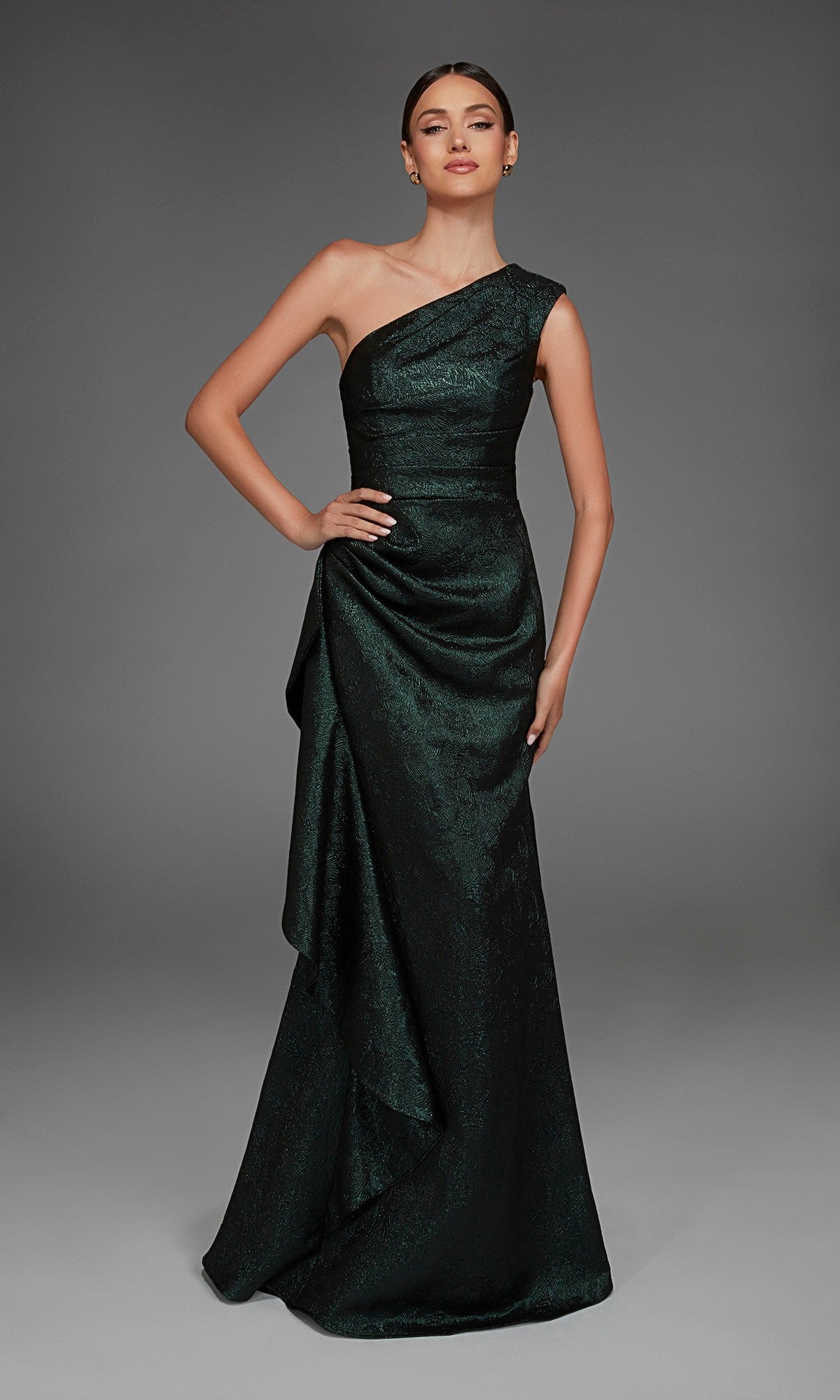A woman wearing the Alyce 27885 long formal dress, a dark green one-shoulder gown with a draped skirt, stands against a plain gray background.