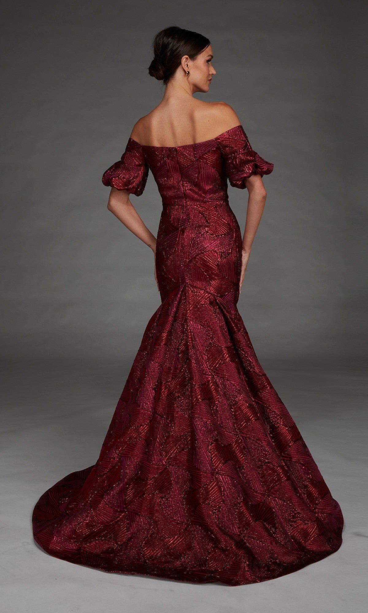 A woman stands against a plain gray background, facing away from the camera, wearing the Alyce 27889 long formal dress. This off-the-shoulder mermaid gown in burgundy features a sweetheart neckline and textured jacquard patterns that elegantly accentuate her silhouette with its fitted mermaid skirt.