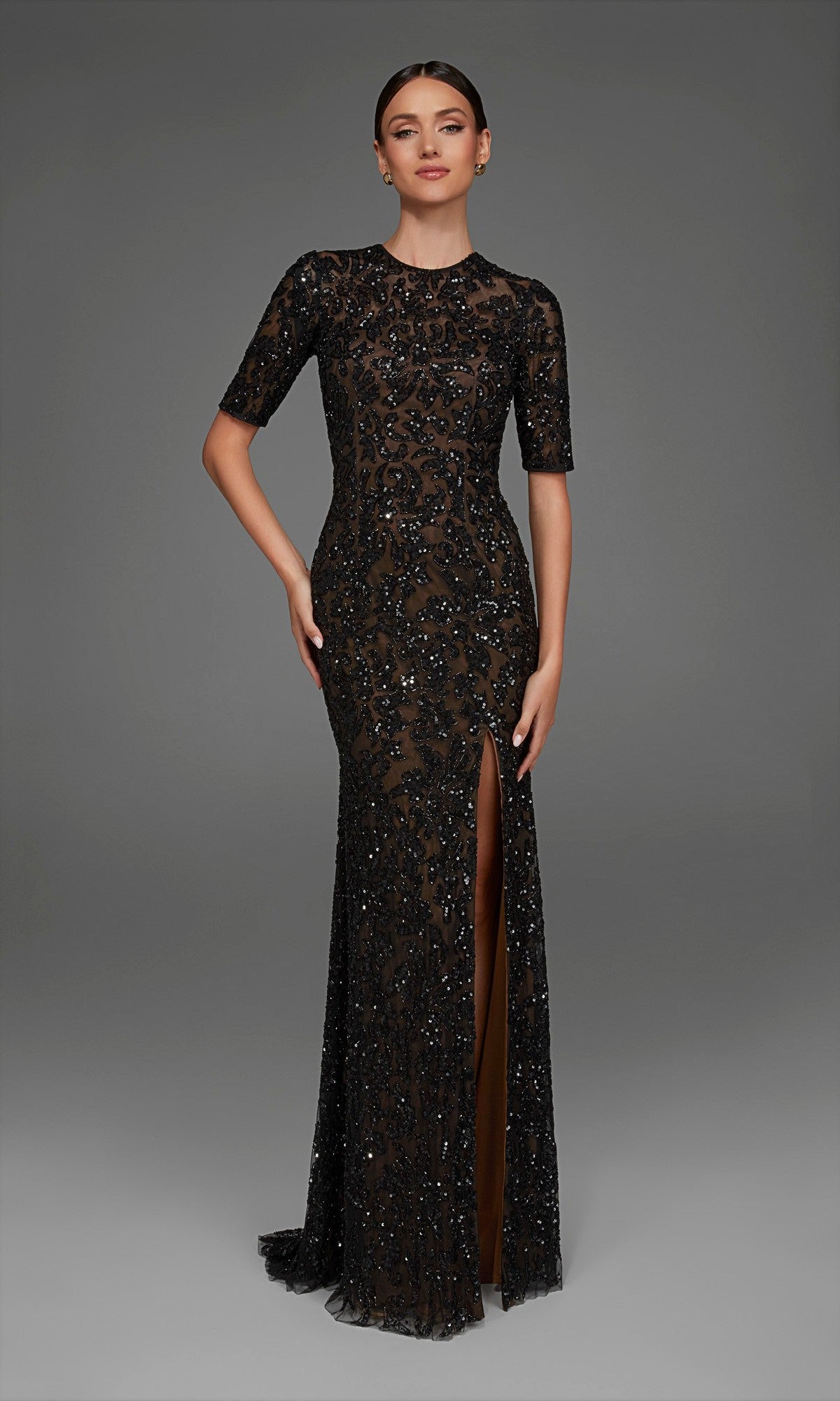 A woman stands against a plain gray background, wearing the Long Formal Dress: Alyce 27901 in Black/Blush—a beaded, floor-length evening gown with short sleeves, a thigh-high front slit, and a fitted column silhouette.