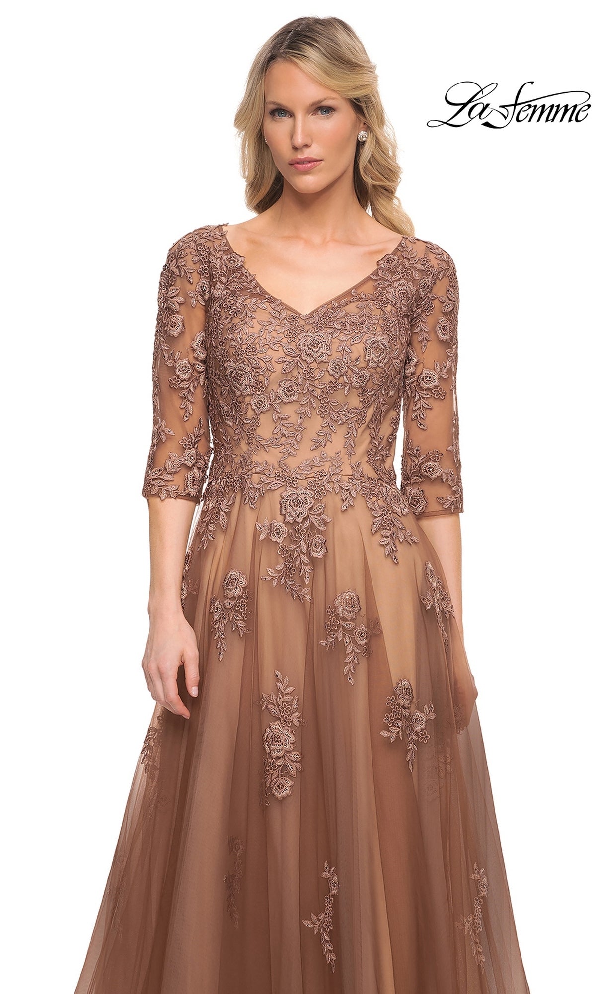 A woman wears the Long Formal Dress: La Femme 27908, a brown lace V-neck evening gown with elbow-length sleeves, floral embroidery, and a full skirt.