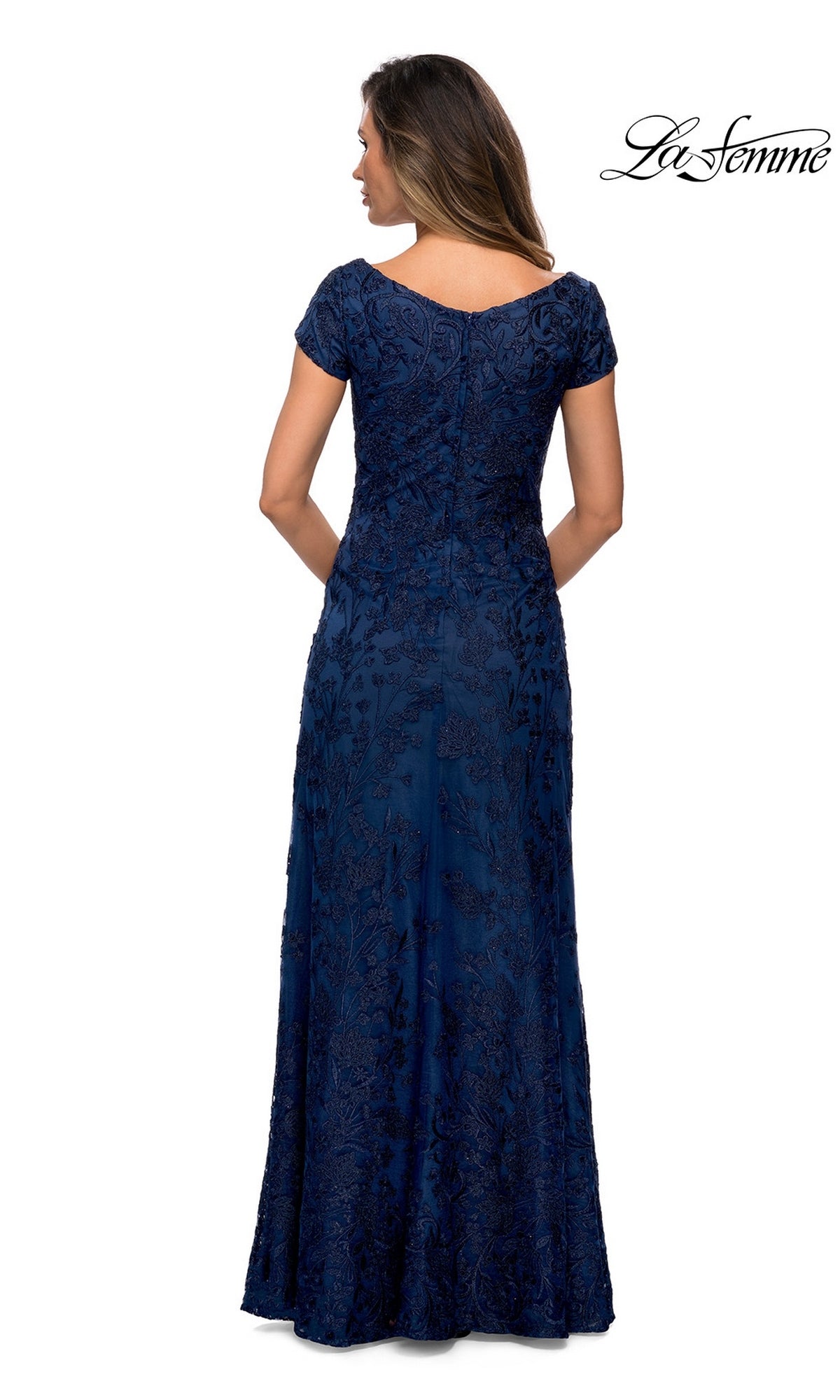 A woman facing away wears the Long Formal Dress: La Femme 27915, a floor-length, short-sleeve navy blue gown with floral patterns. “La Femme” logo at top right on white background.