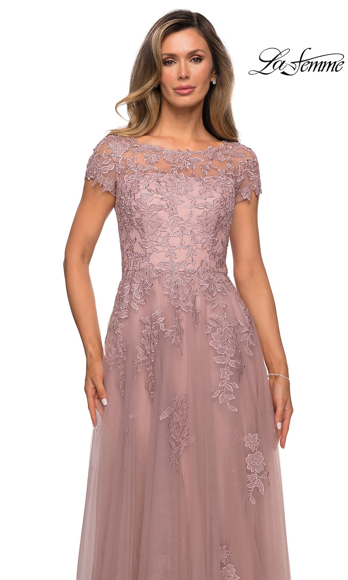 Woman wearing the Long Formal Dress: La Femme 27920, a mauve, short-sleeve, floor-length floral lace A-line dress with embroidery, stands against a white background.
