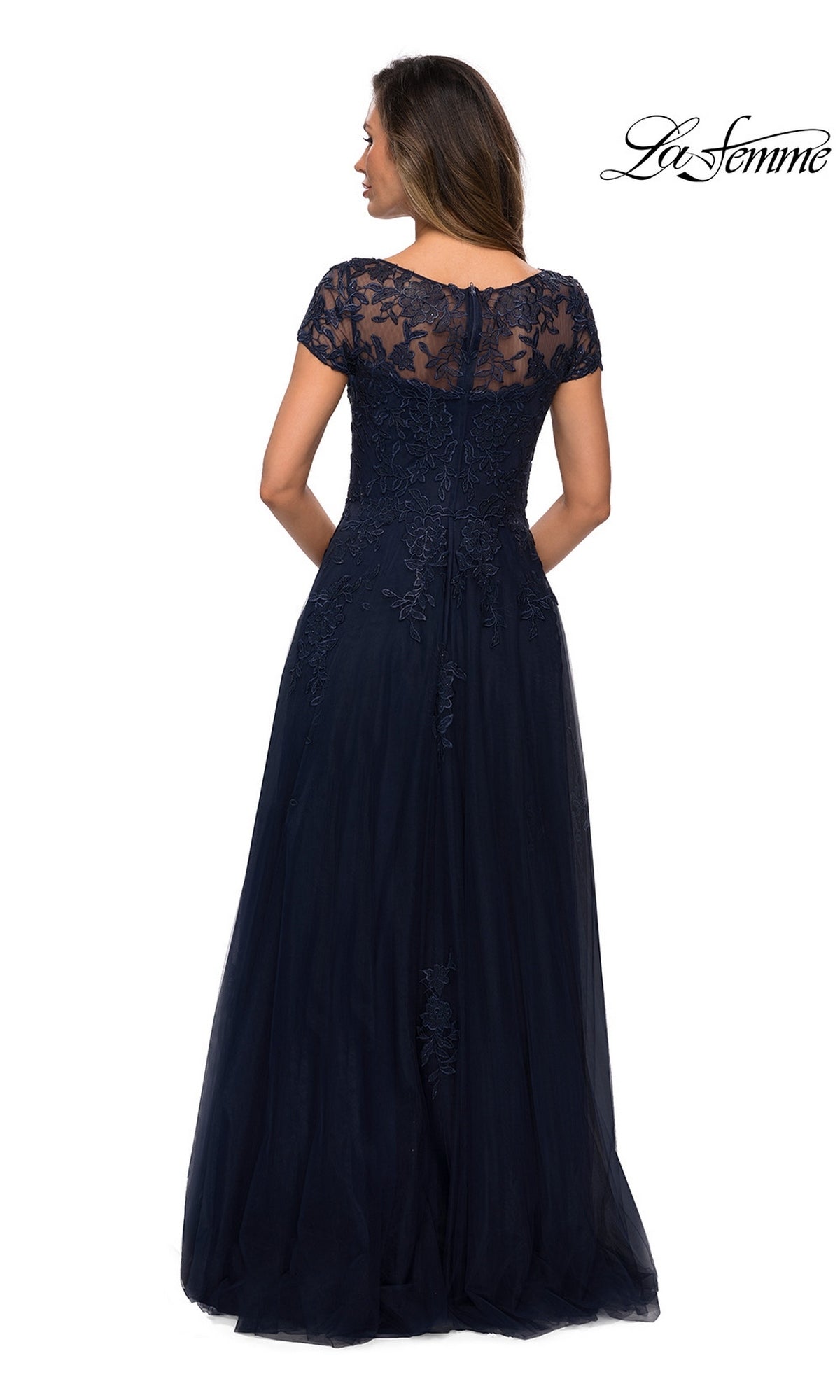 Woman in a floor-length, navy blue “Long Formal Dress: La Femme 27920” with floral lace short sleeves and sheer lace back, facing away; “La Femme” logo at top right.