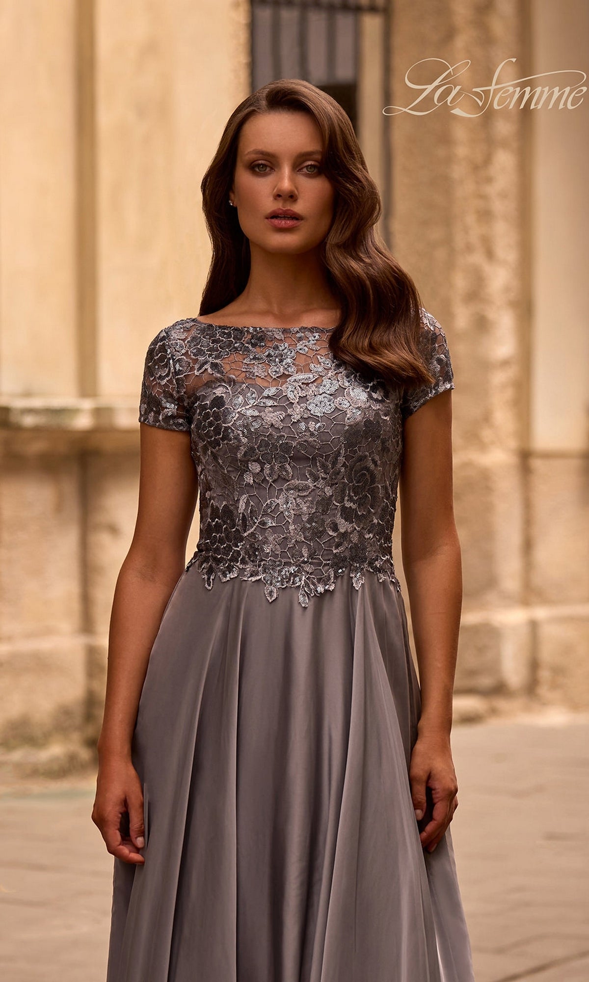 Woman in Long Formal Dress: La Femme 27924 with a metallic-lace bodice stands outdoors, ideal for a mother-of-the-bride look.