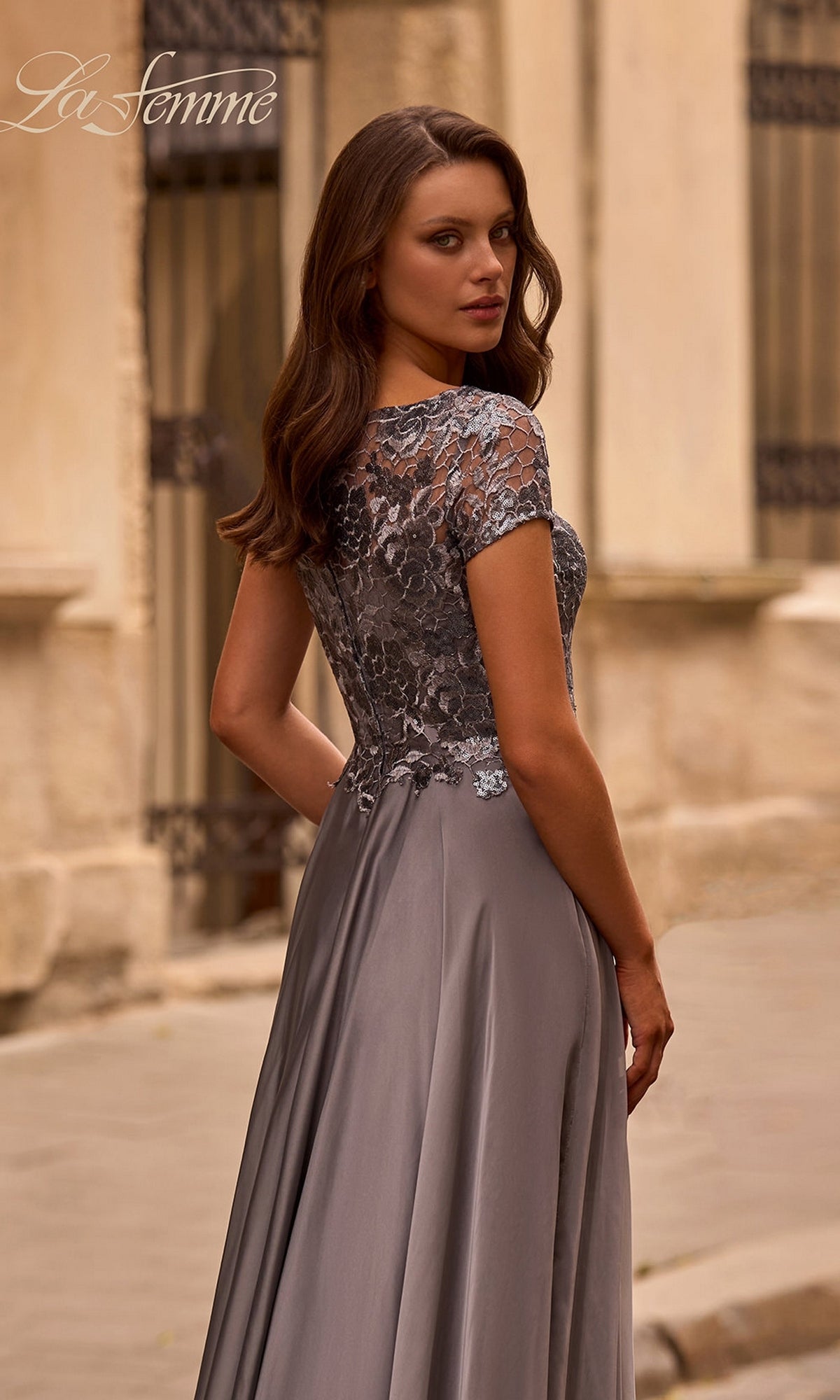 Woman in the Long Formal Dress: La Femme 27924 with a metallic-lace bodice, standing outdoors and looking over her shoulder—ideal for mother-of-the-bride.