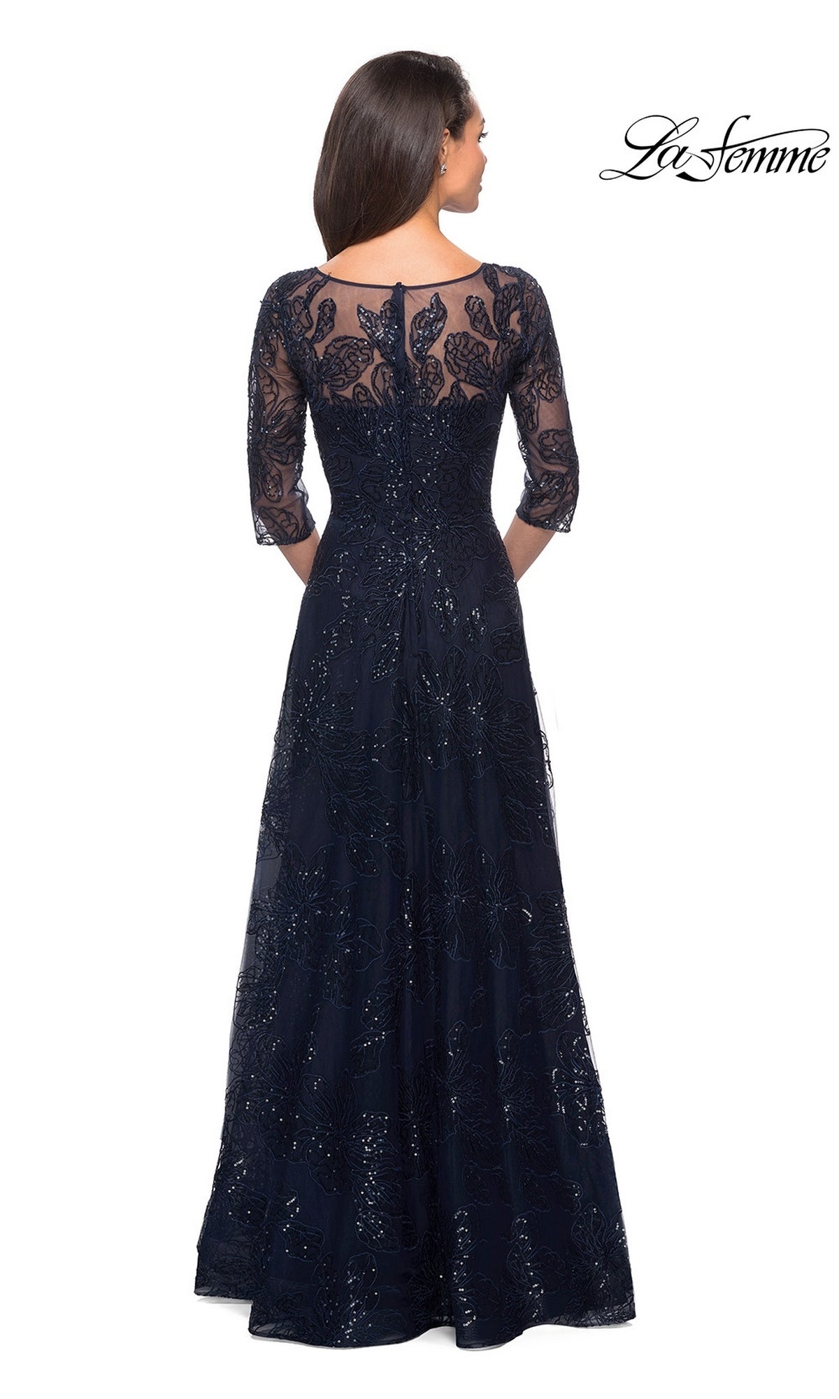 A woman faces away in the Long Formal Dress: La Femme 27942, a floor-length sequined lace gown with three-quarter sleeves, sheer back, and elegant floral patterns.