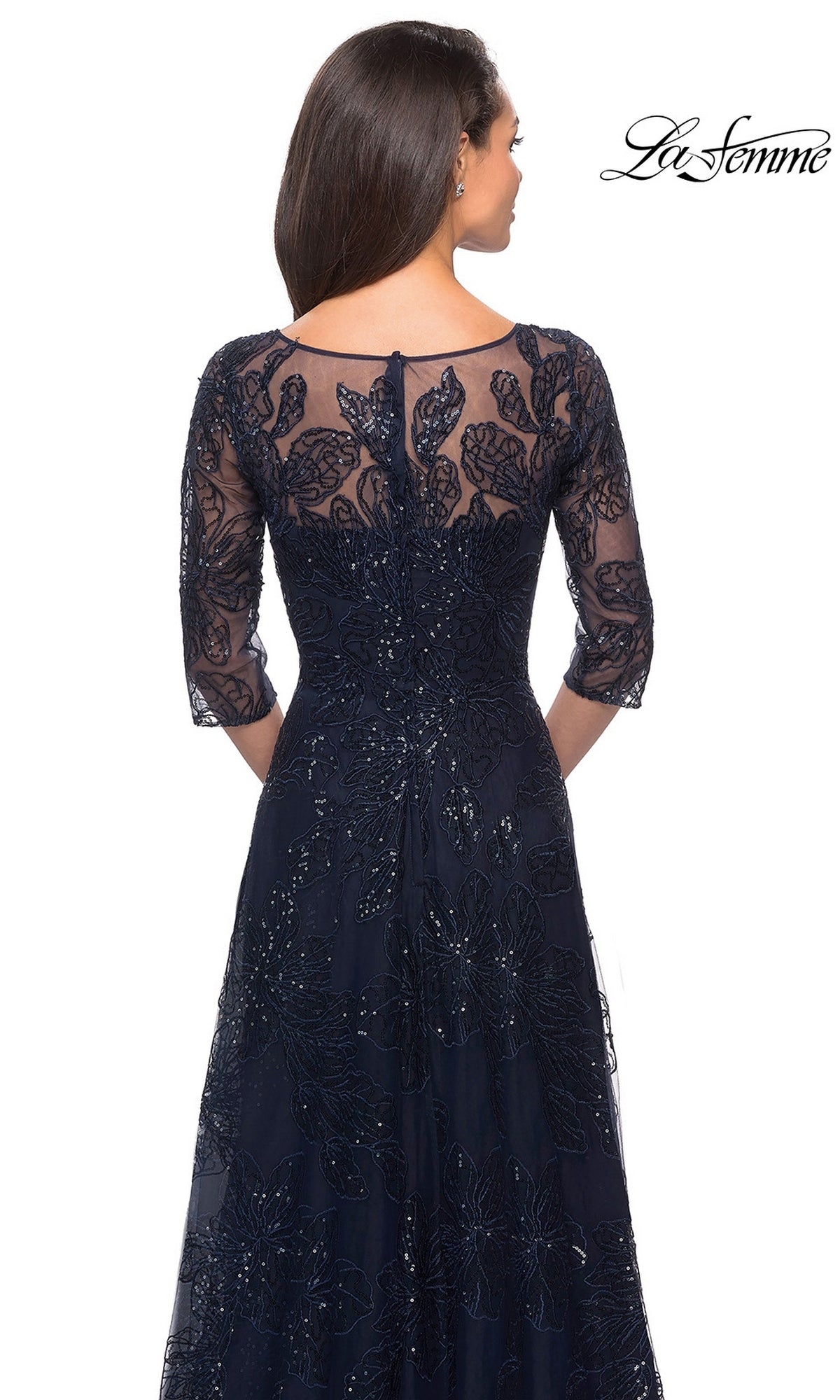 Woman in a Long Formal Dress: La Femme 27942, navy blue floral A-line gown with sheer lace and sequins, seen from the back—a stunning modest formal look.