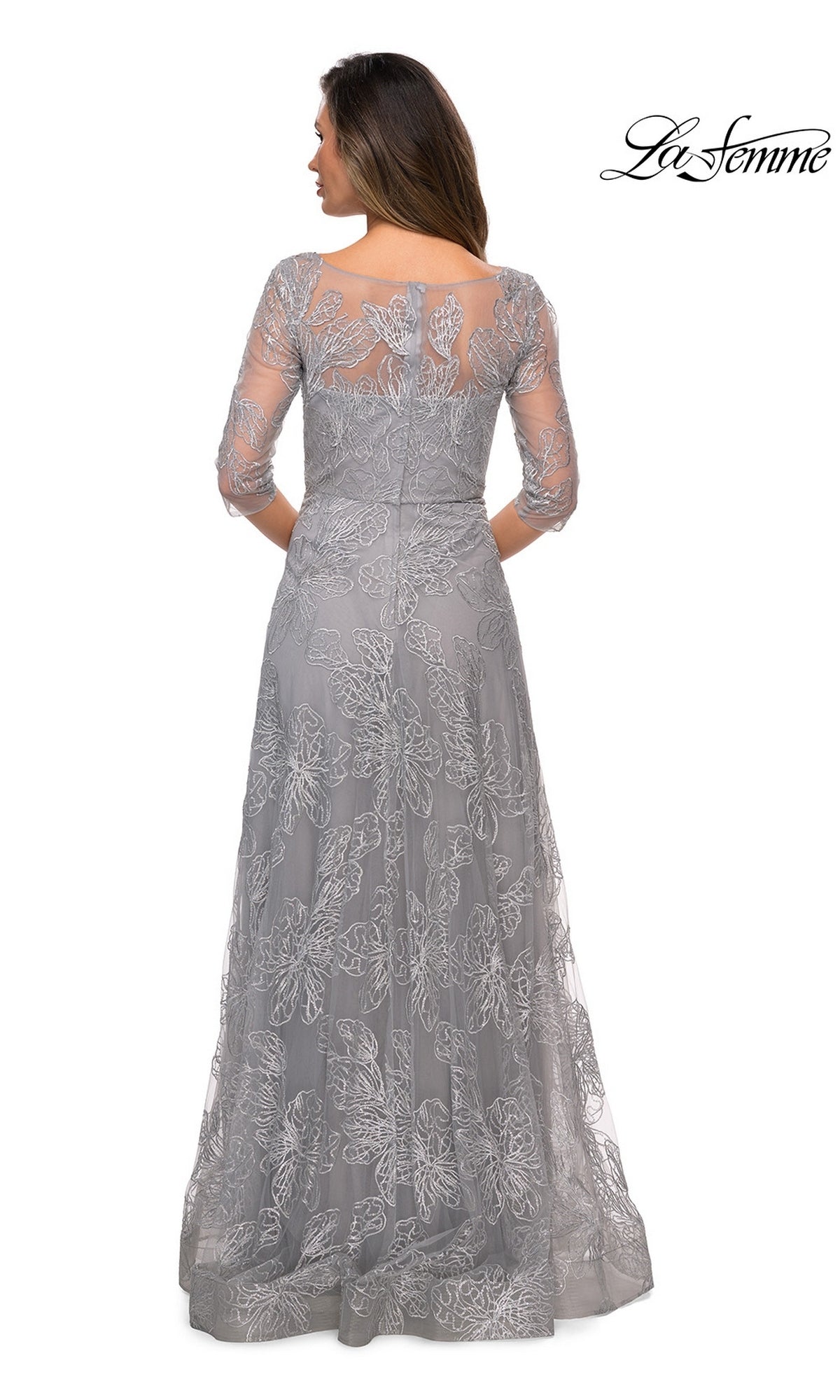 Woman facing away in Long Formal Dress: La Femme 27942—a floor-length silver sequined lace gown with three-quarter sleeves and sheer back. “La Femme” logo top right.