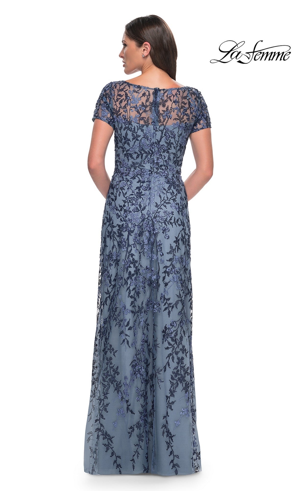 A woman stands with her back to the camera, wearing the Long Formal Dress: La Femme 27956, a blue lace evening gown with floral beaded details.