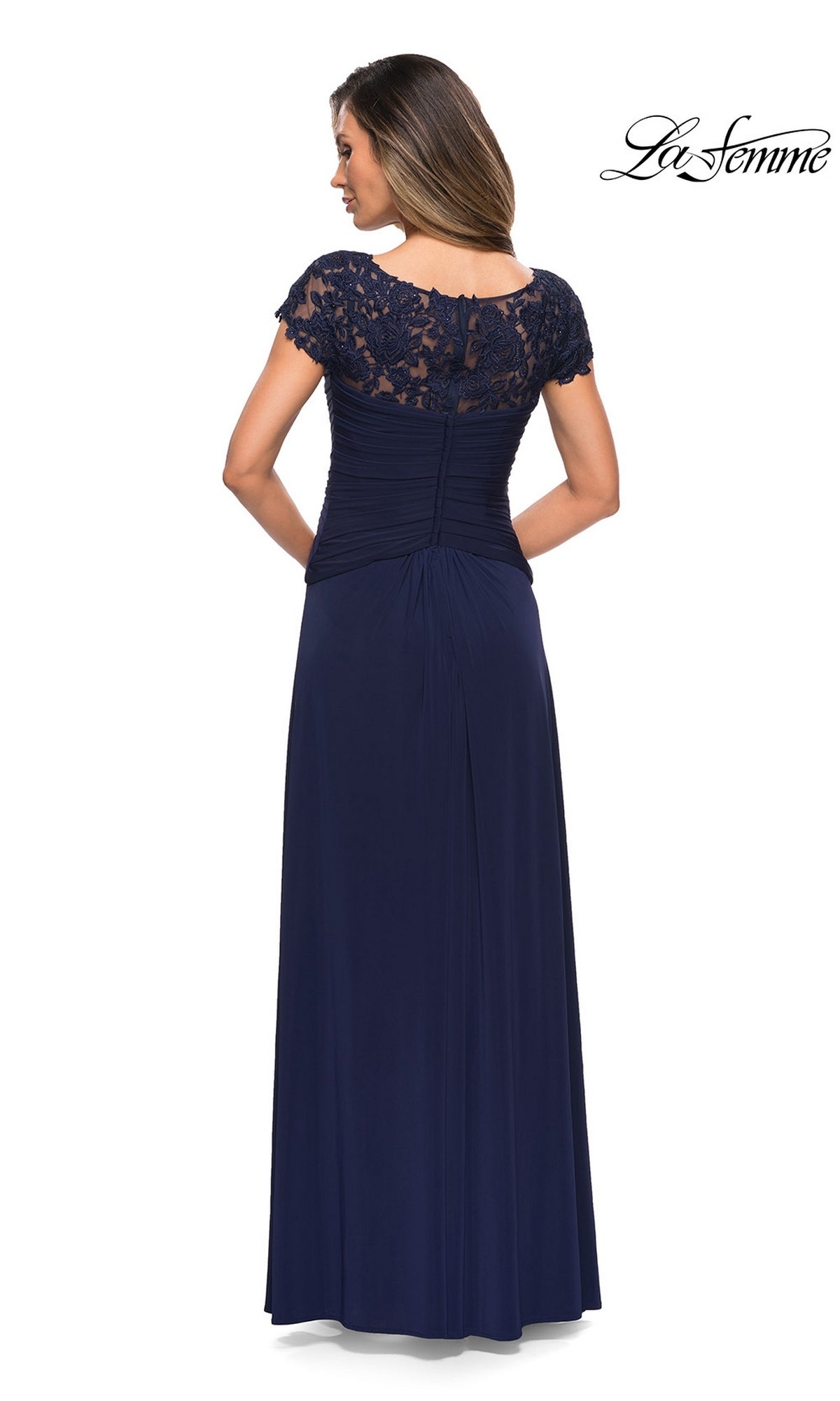 Woman in the Long Formal Dress: La Femme 28029 poses, highlighting its navy lace cap sleeves, gathered waist, A-line skirt, and back keyhole detail.