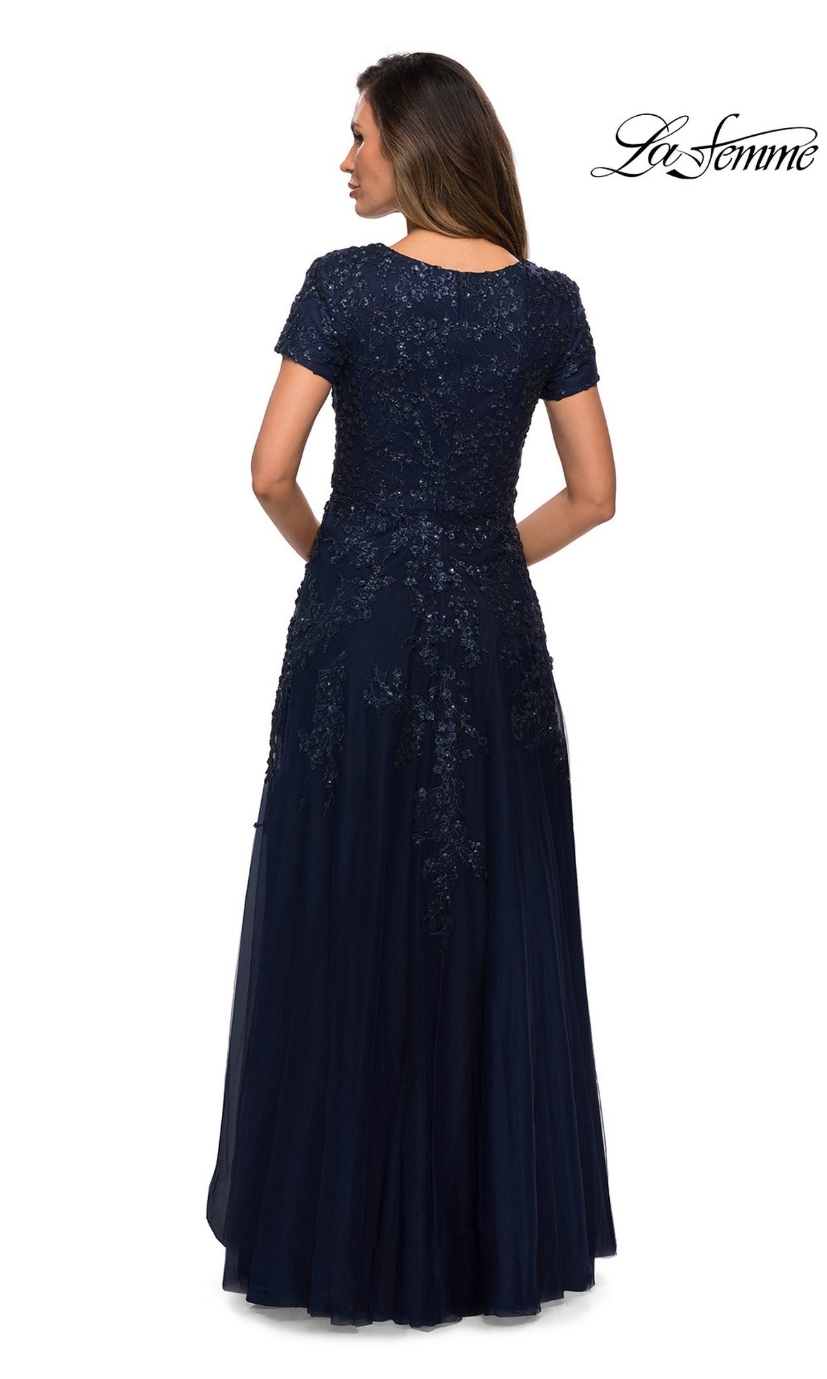 A woman wearing the Long Formal Dress: La Femme 28037, seen from behind in a navy blue, floor-length A-line tulle gown with beaded appliques on the lace and sequin bodice and hips.