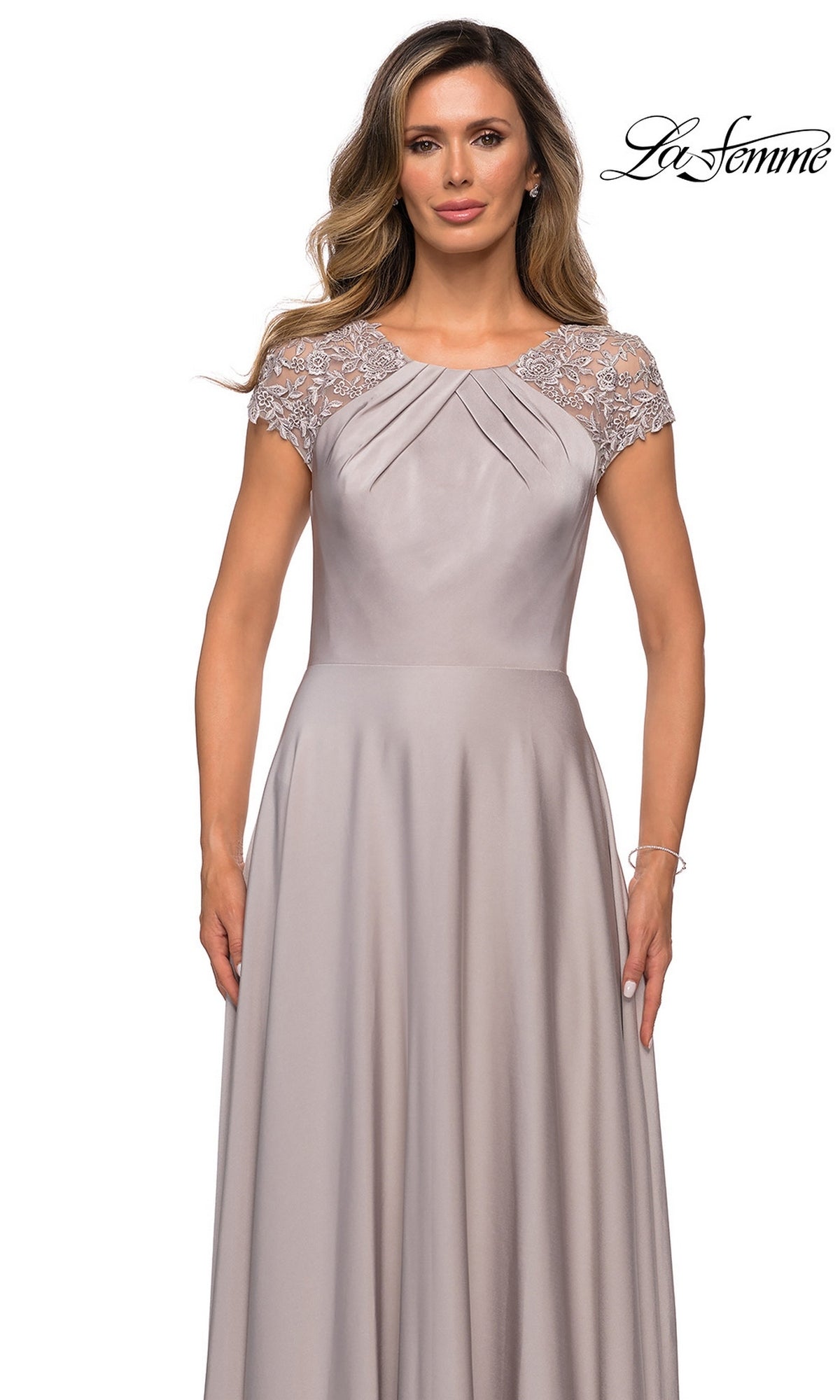 A woman wearing the Long Formal Dress: La Femme 28100, a light gray, floor-length gown with an elegant A-line silhouette, lace cap sleeves, and pleated bodice detail, stands against a white background.