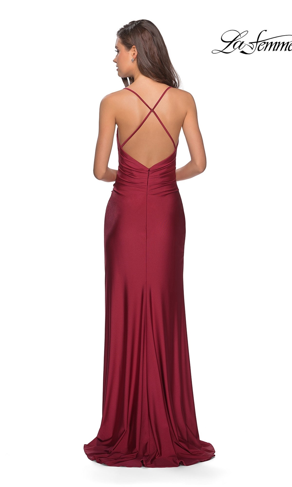 A woman stands against a white background wearing the La Femme Open-Back Long V-Neck Prom Dress 28206, a floor-length burgundy gown with a sleeveless design, low open back, and crisscross straps.