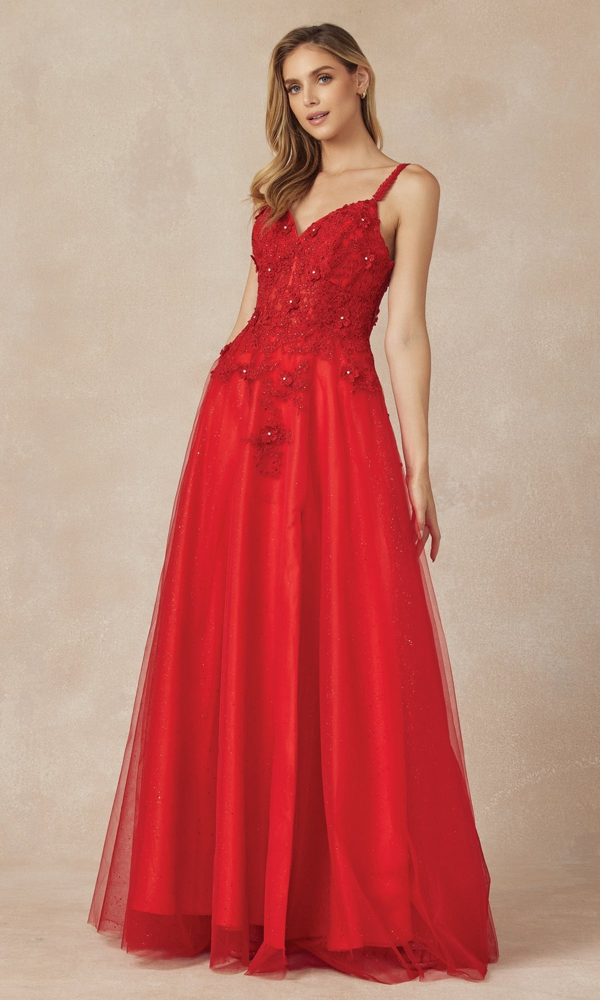 A woman stands wearing the Long Prom Dress 283 by Juliet, a floor-length, sleeveless red A-line gown with floral lace embroidery on the bodice and a graceful V-neckline, set against a neutral background.