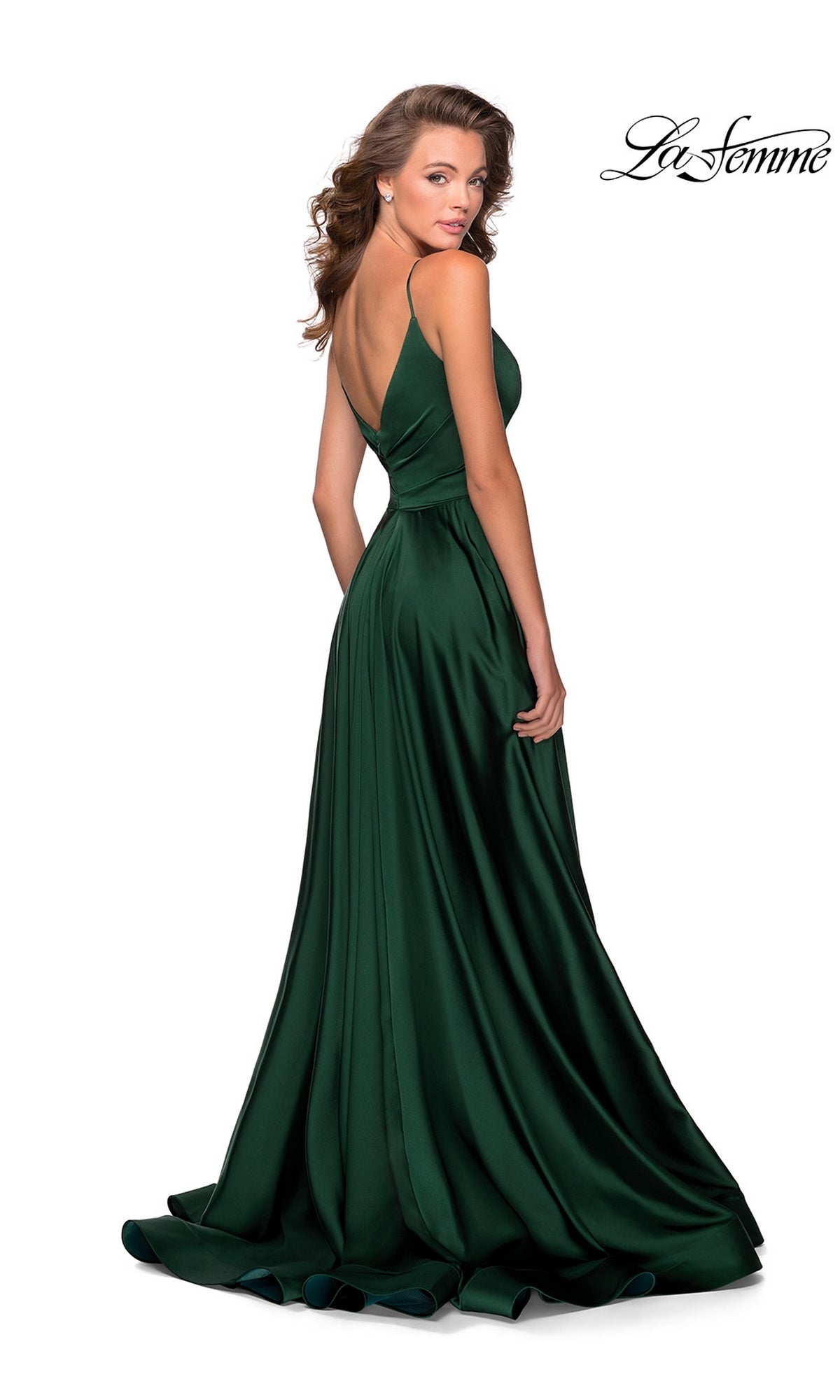 Woman in a deep green La Femme V-Neck Long A-Line Prom Dress 28607 with a V-back, standing and looking over her shoulder. This gown features a fitted bodice and a floor-length flowing skirt.