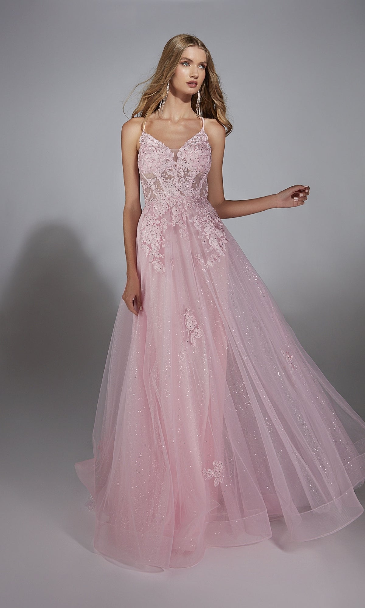 A woman models the Glitter Tulle Prom Ball Gown: Aerie Couture 286—a long, light pink dress with a corset back, floral lace accents, and a tulle skirt—standing against a plain gray background.