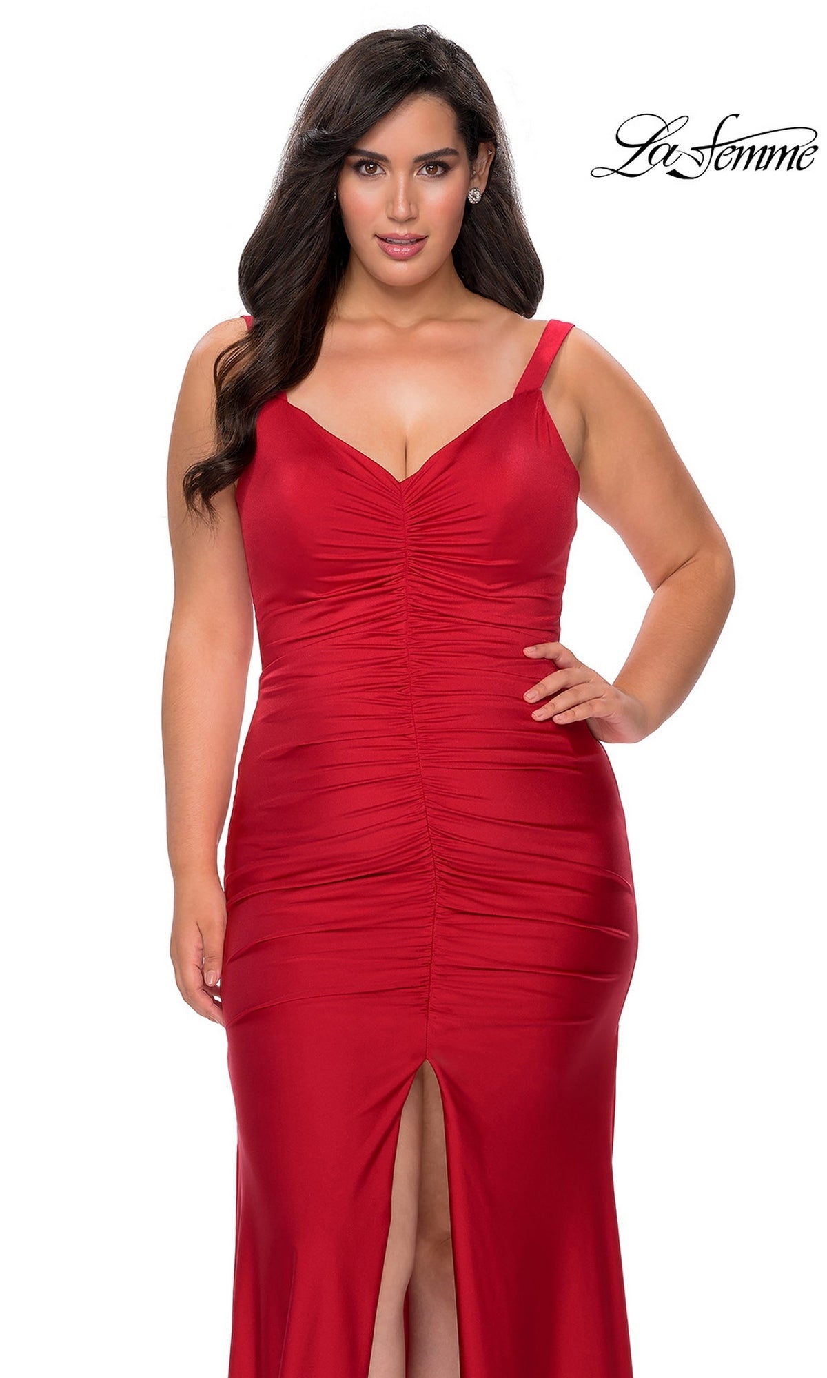 A woman wears a long, red, ruched jersey Long Plus-Size Prom Dress: La Femme 29027 featuring a V-neck bodice and a front slit.