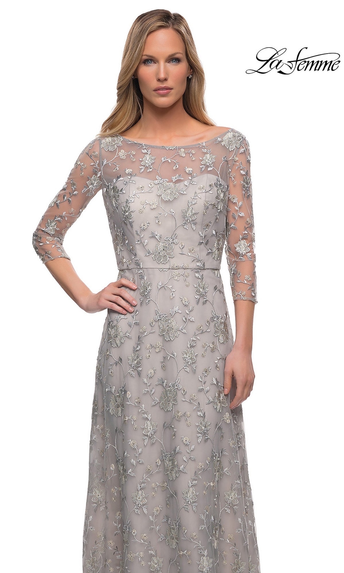 Woman in Long Formal Dress: La Femme 29153—silver gown with floral lace embroidery, sheer three-quarter sleeves, and fitted bodice. “La Femme” logo at the top right corner.