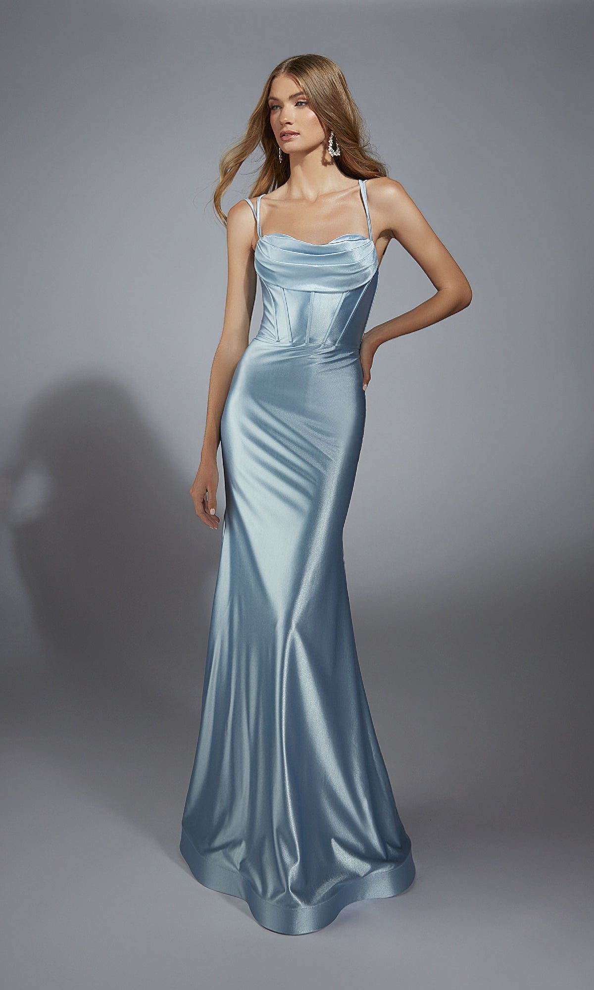 A woman in the Aerie Couture 291 long prom dress, featuring light blue satin fabric, thin straps, a fitted corset bodice, and a subtle mermaid silhouette, stands against a plain gray background.