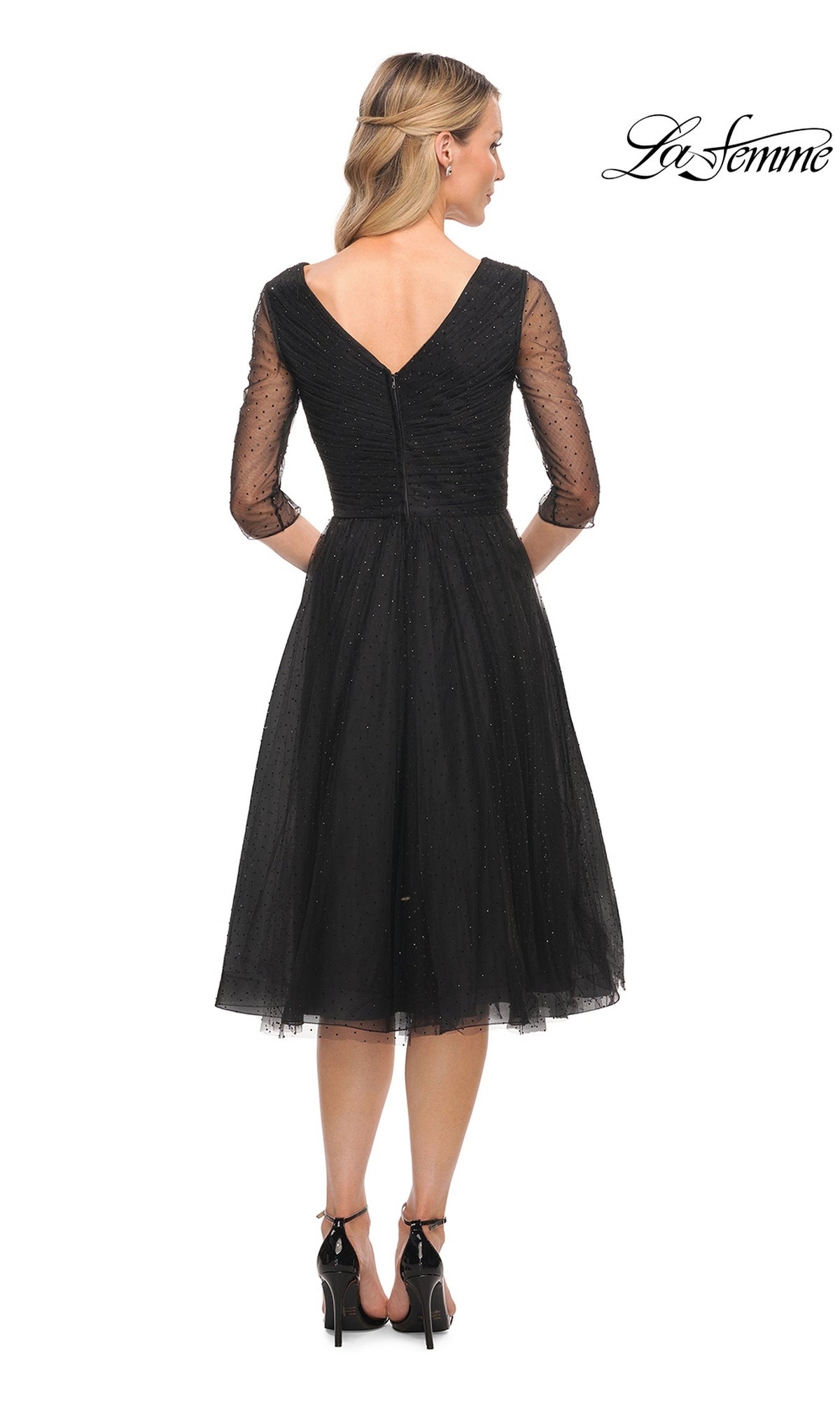 Woman in Knee Length Wedding Guest Dress: La Femme 29229 with sheer three-quarter sleeves and v-neck back, paired with black heels.