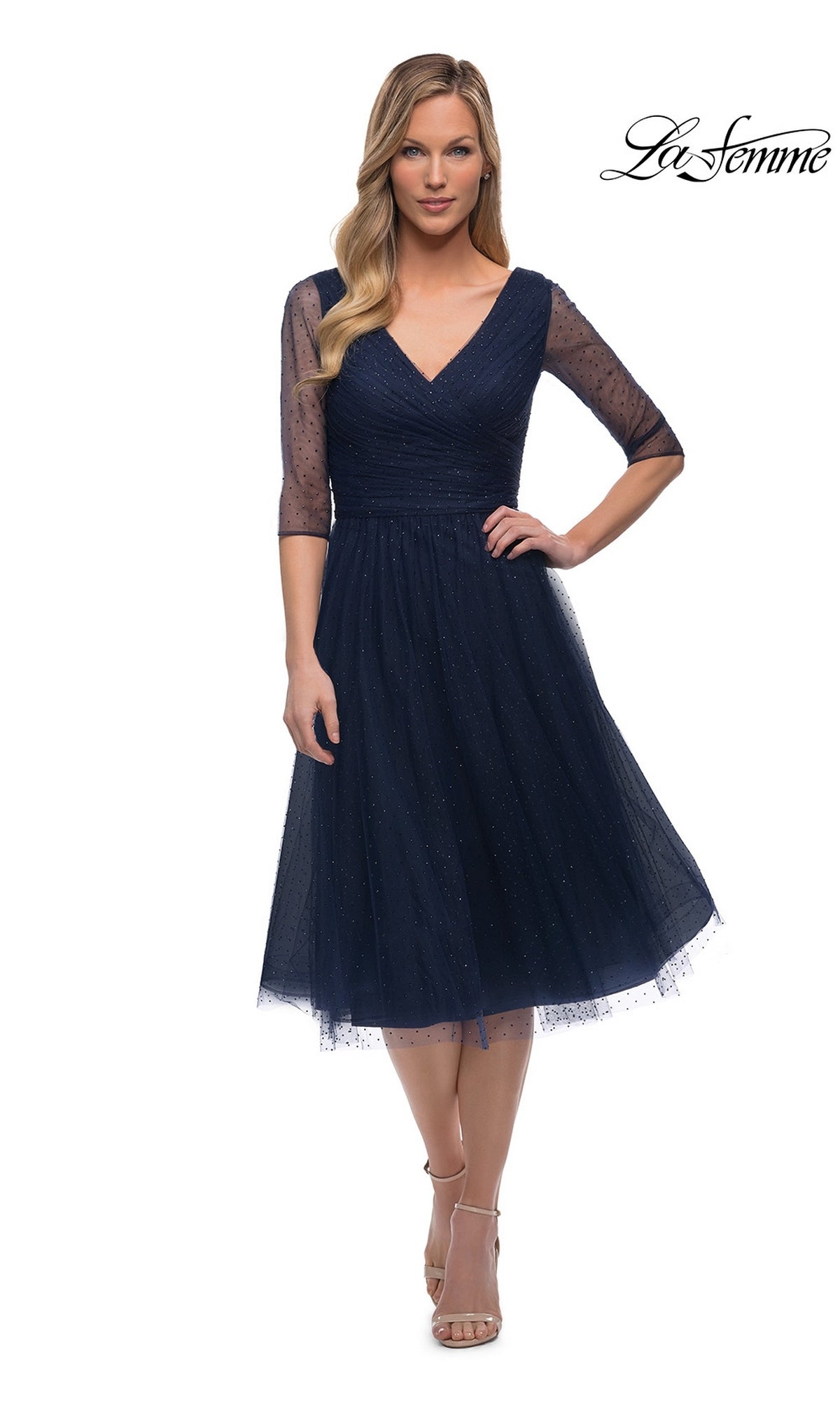 Woman wearing the Knee Length Wedding Guest Dress: La Femme 29229 in navy, featuring sheer three-quarter sleeves and sparkly accents, paired with neutral heels.