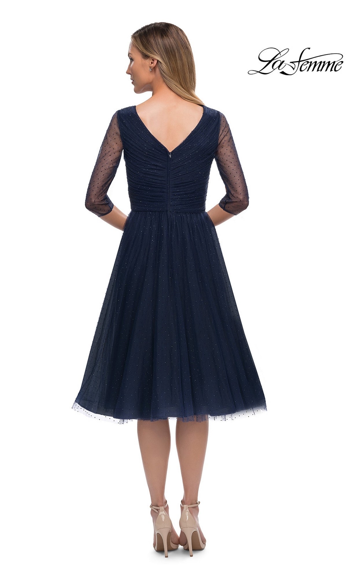 Woman wearing the Knee Length Wedding Guest Dress: La Femme 29229 in navy blue with sheer three-quarter sleeves, v-neckline, and V-back, paired with high heels.
