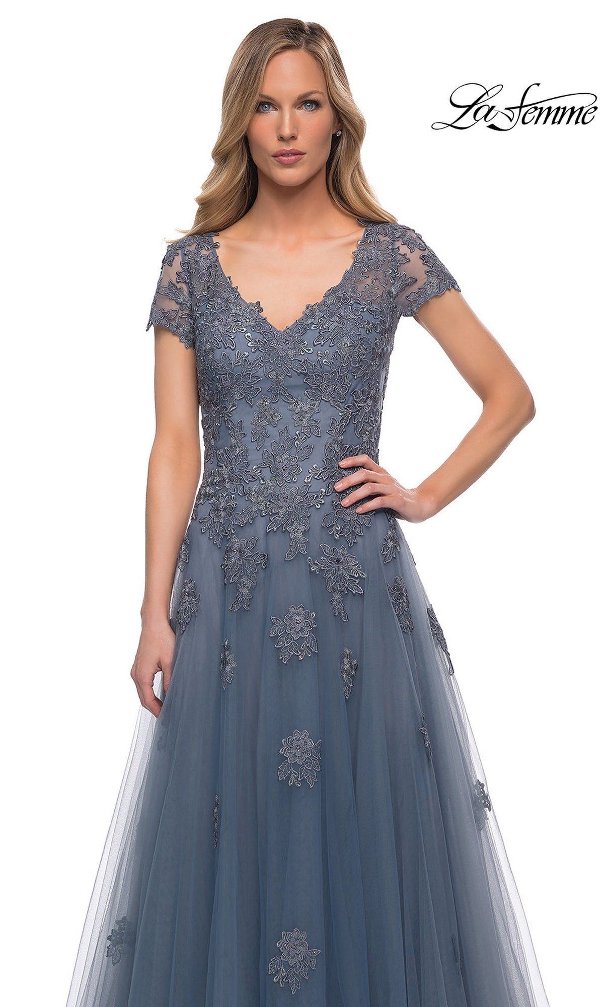 Woman wearing Long Formal Dress: La Femme 29380—slate blue, floor-length tulle with lace appliqué, short sleeves, V-neck—posing against a white background. “La Femme” logo top right.