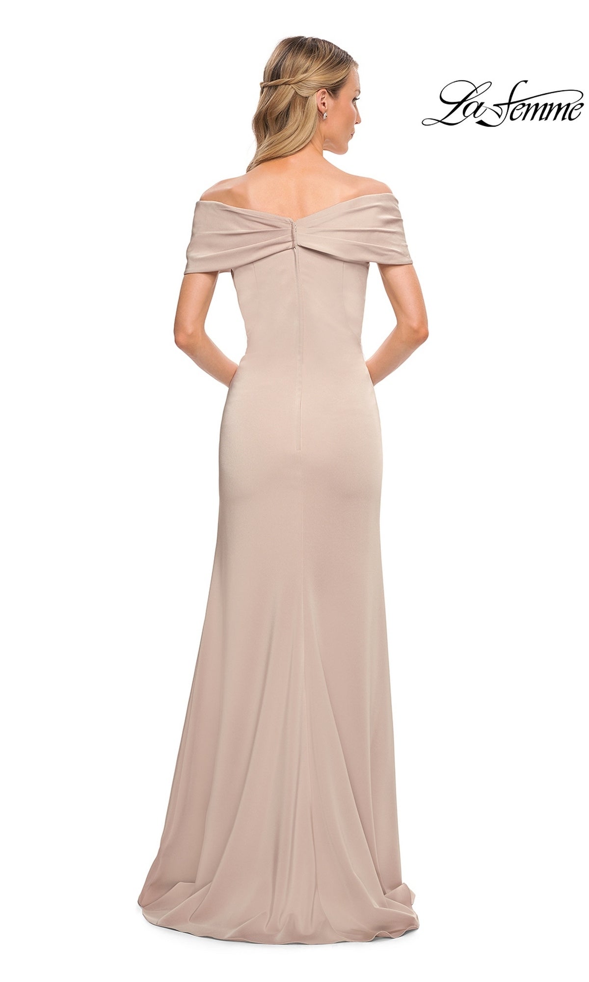 A woman models the Long Formal Dress: La Femme 29537, an off-the-shoulder, floor-length light beige gown. The fitted sheath design elegantly highlights her silhouette as she faces away, revealing the back details of the dress. The “La Femme” logo appears in the top right corner.
