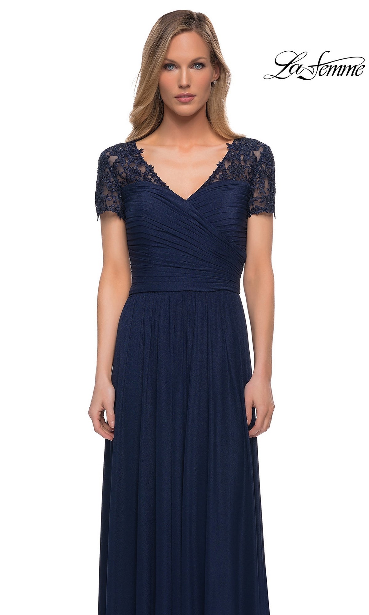 A woman in the Long Formal Dress: La Femme 29772 poses against a white background, navy blue with lace short sleeves and a ruched fitted bodice. “La Femme” logo at top right.